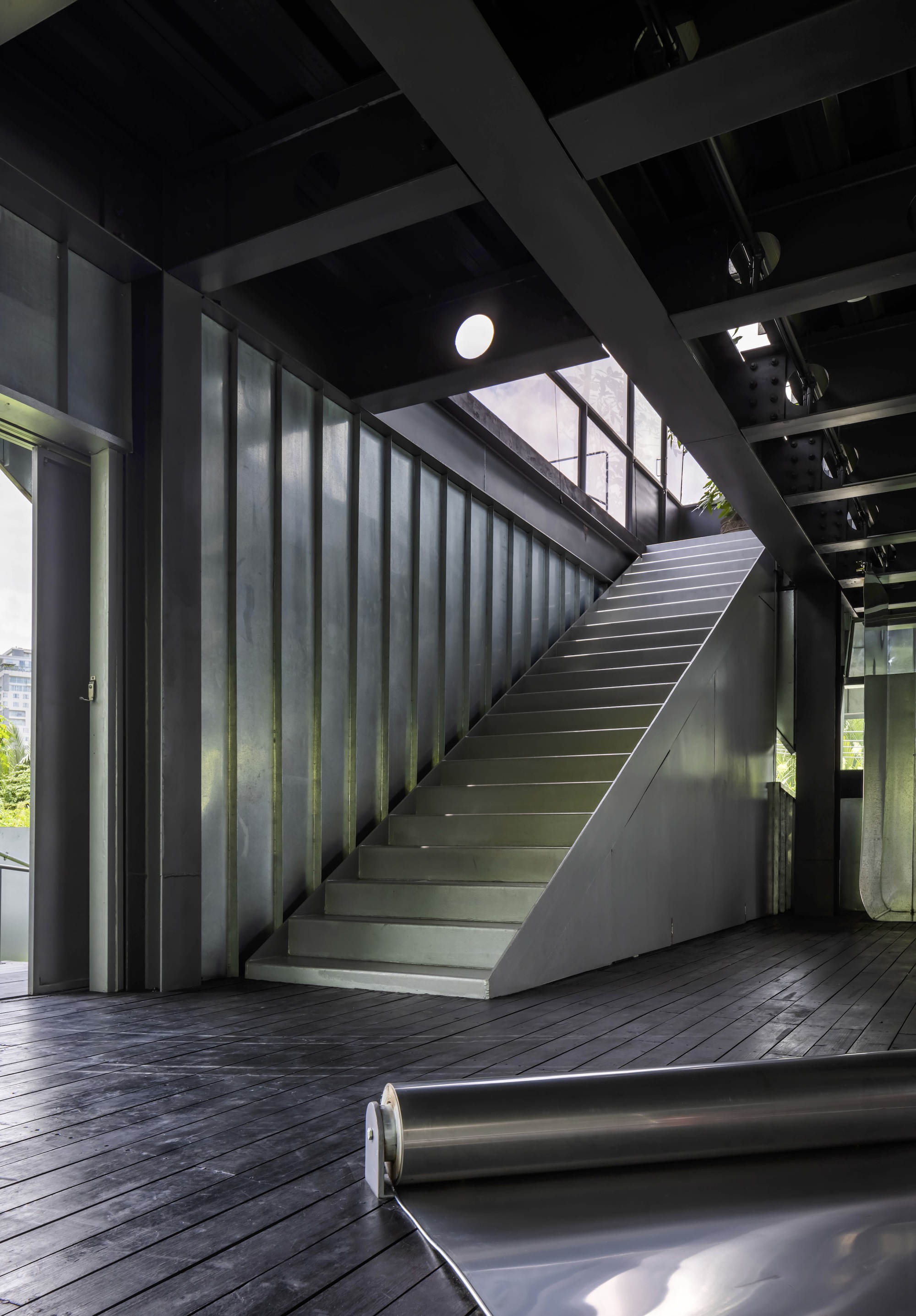 Interior staircase with blackened steel cladding and timber decking under an exposed beam ceiling