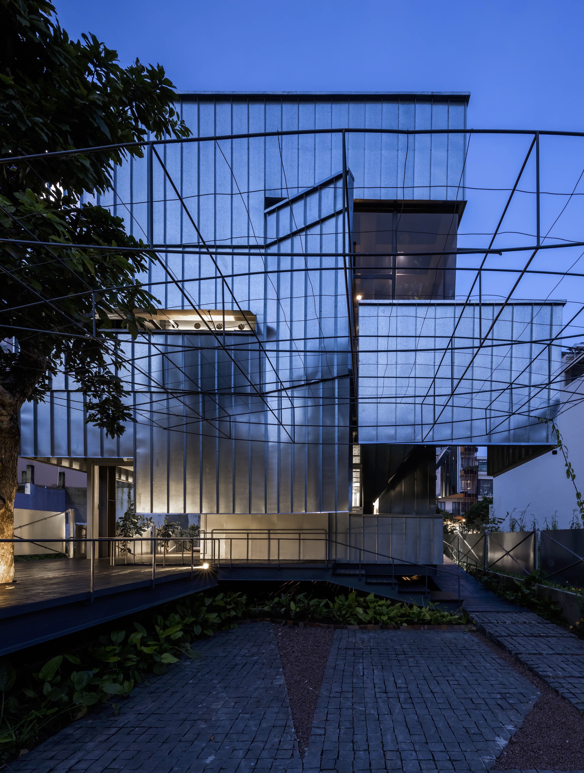 Translucent corrugated facade with steel frame and planted courtyard at dusk