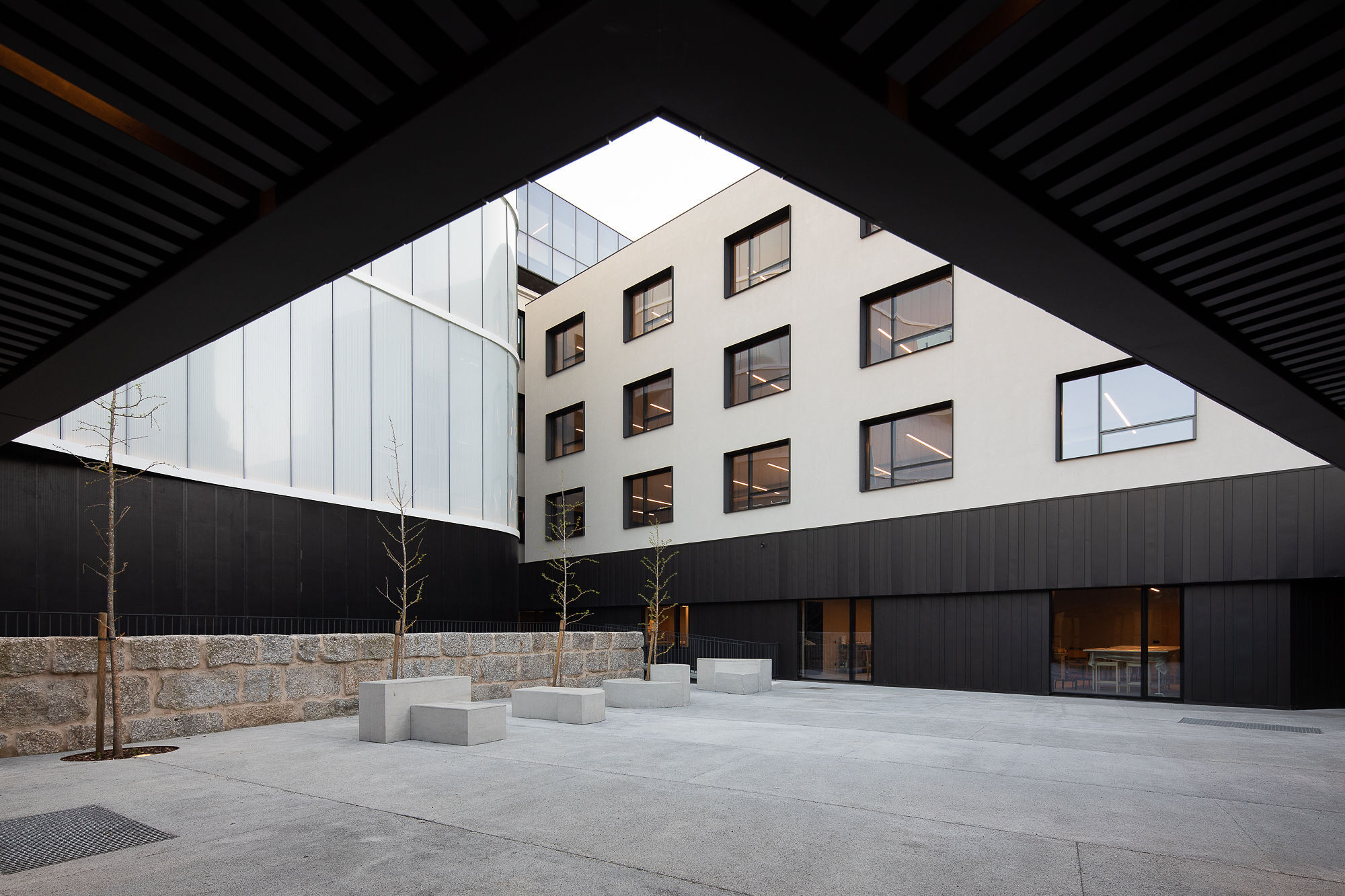 Covered courtyard entry framed by dark slatted ceiling with concrete pavers and young trees below