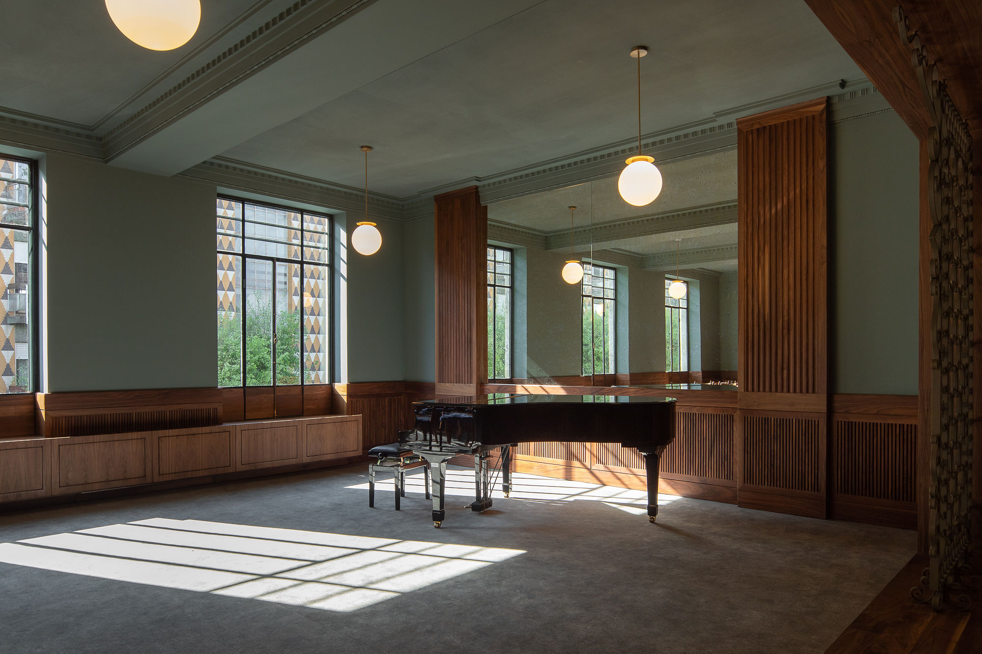 Interior room with grand piano, fluted wood paneling, globe pendant lights and afternoon sunlight streaming across floor