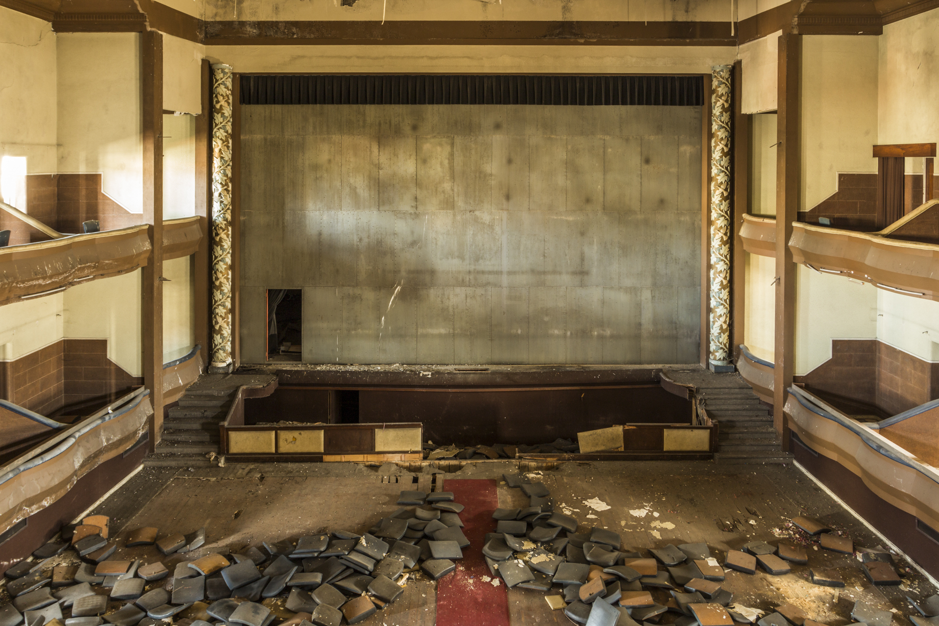 Derelict theater auditorium with tiered seating galleries and ornamental columns flanking the stage
