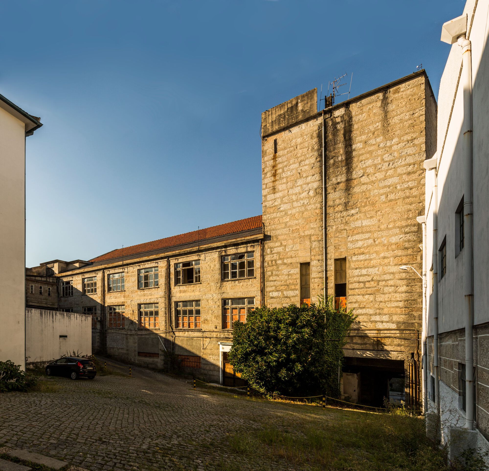 Courtyard view of weathered stone buildings with a tall tower and low wing at golden hour