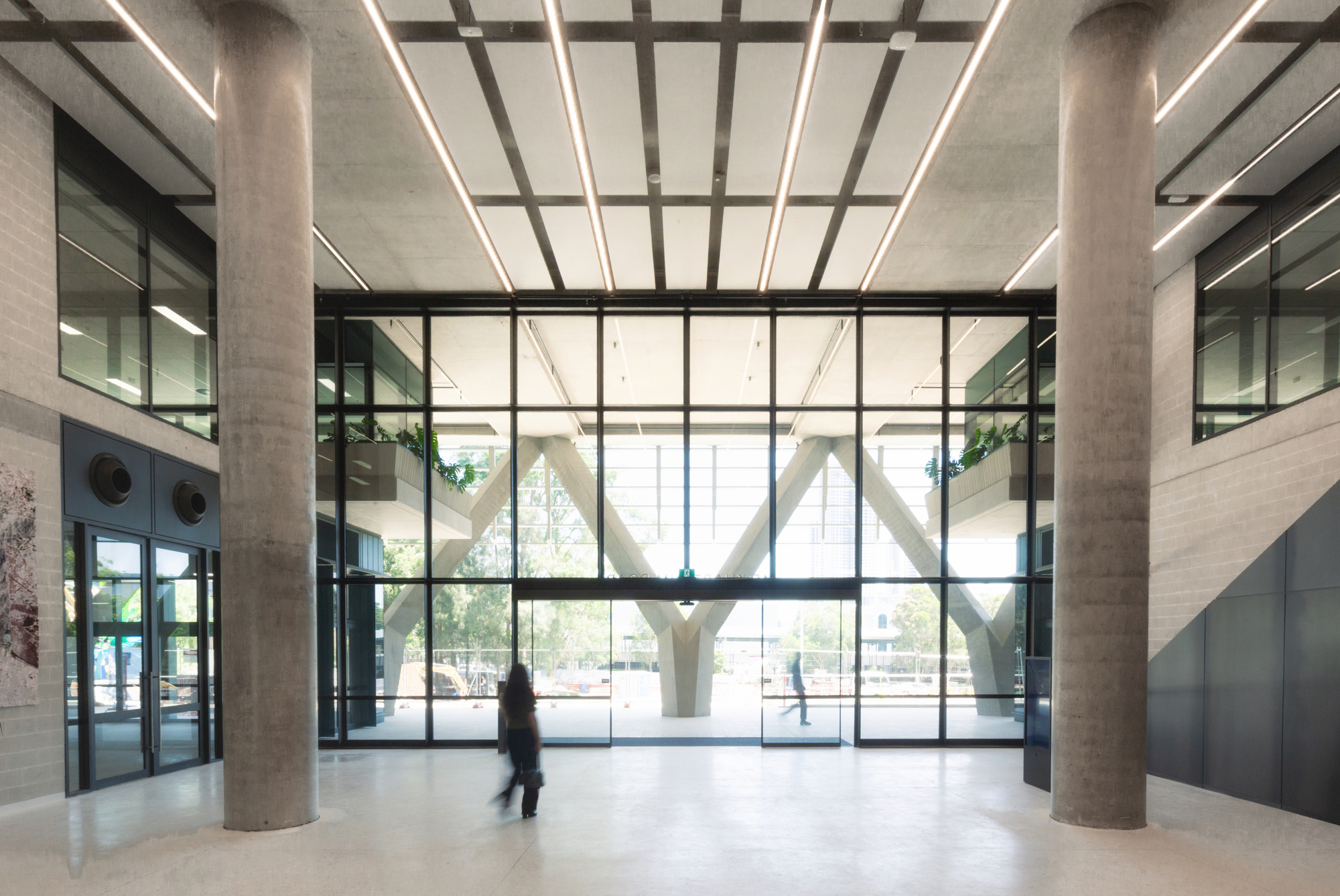 Lobby with concrete ceiling grid and glass walls overlooking the branching columns with a passing figure
