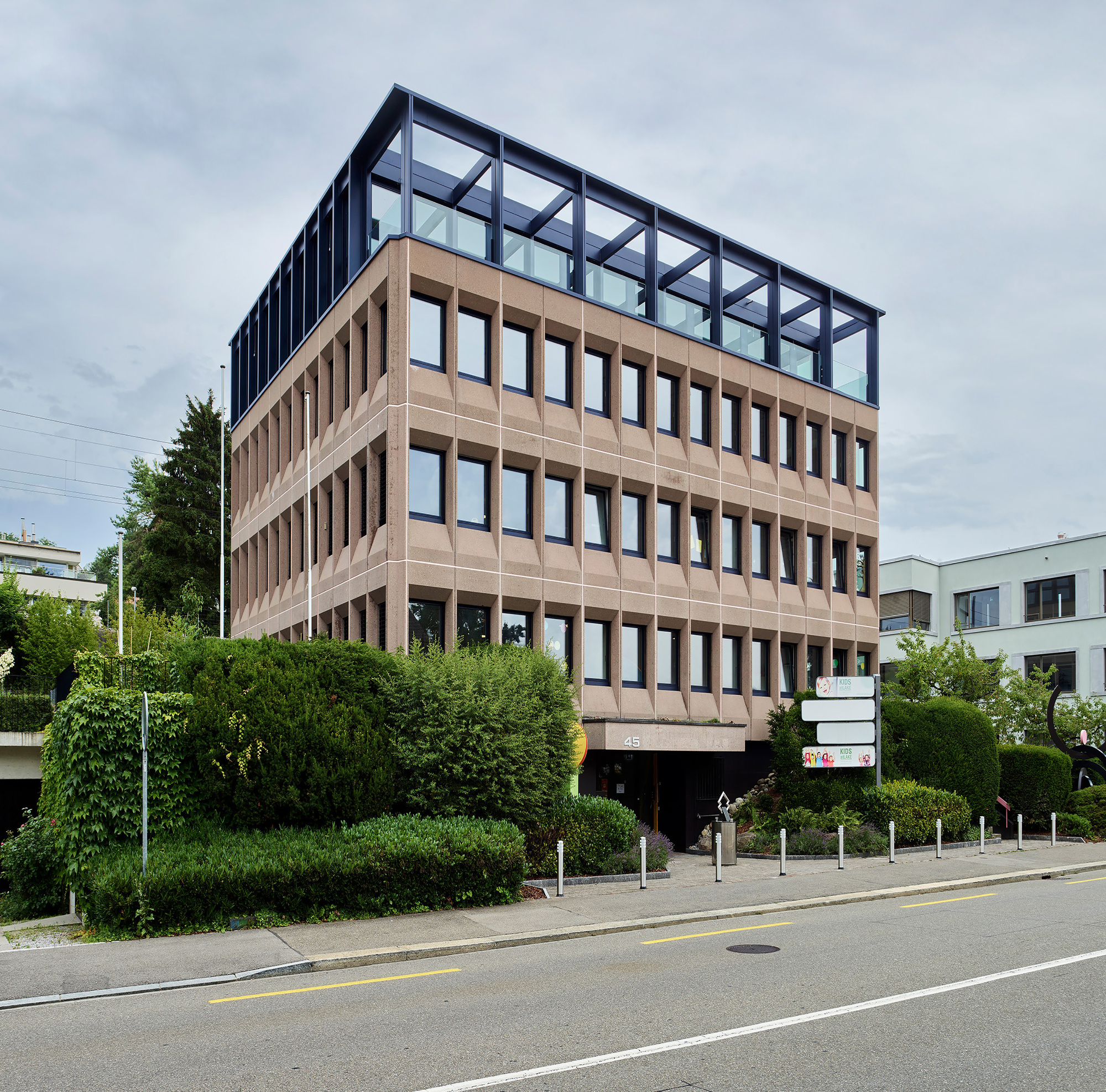 Corner facade showing the stacked terracotta panel system topped by a black steel and glass penthouse volume