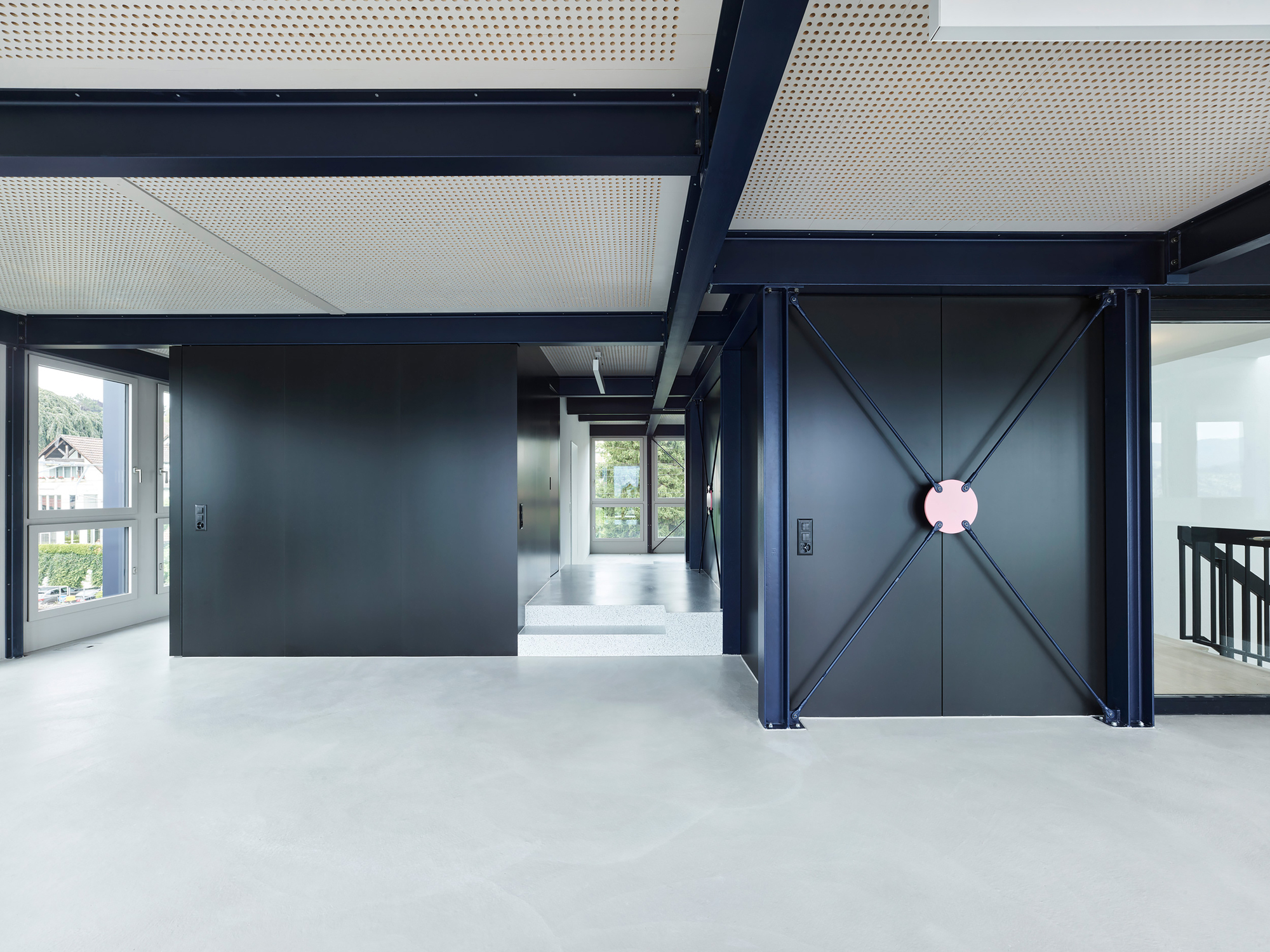 Open plan interior with exposed steel frame, perforated ceiling panels, and black partition walls with gray flooring