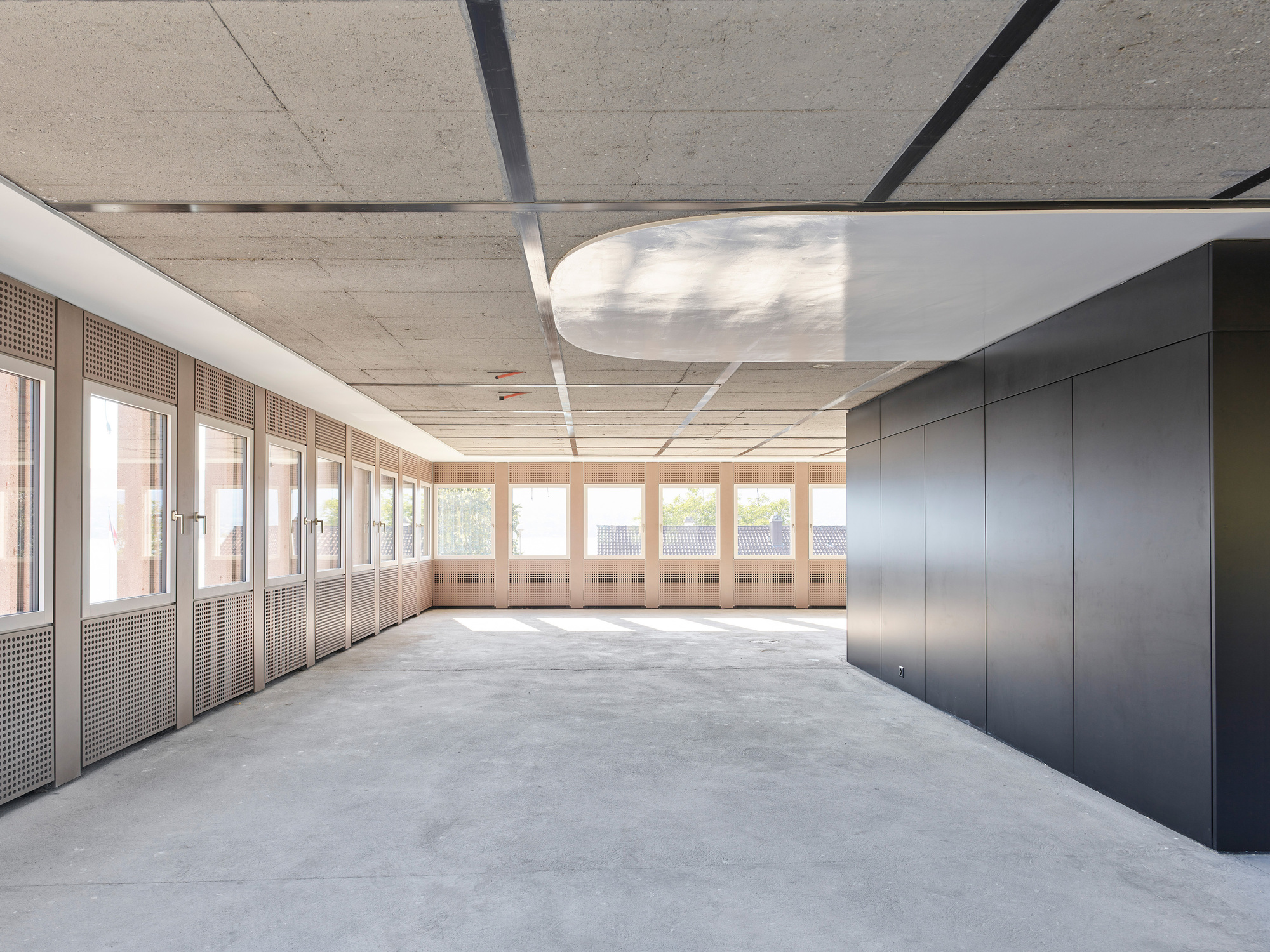 Interior corridor space with concrete ceiling, continuous strip lighting, perforated wall panels, and polished concrete floor
