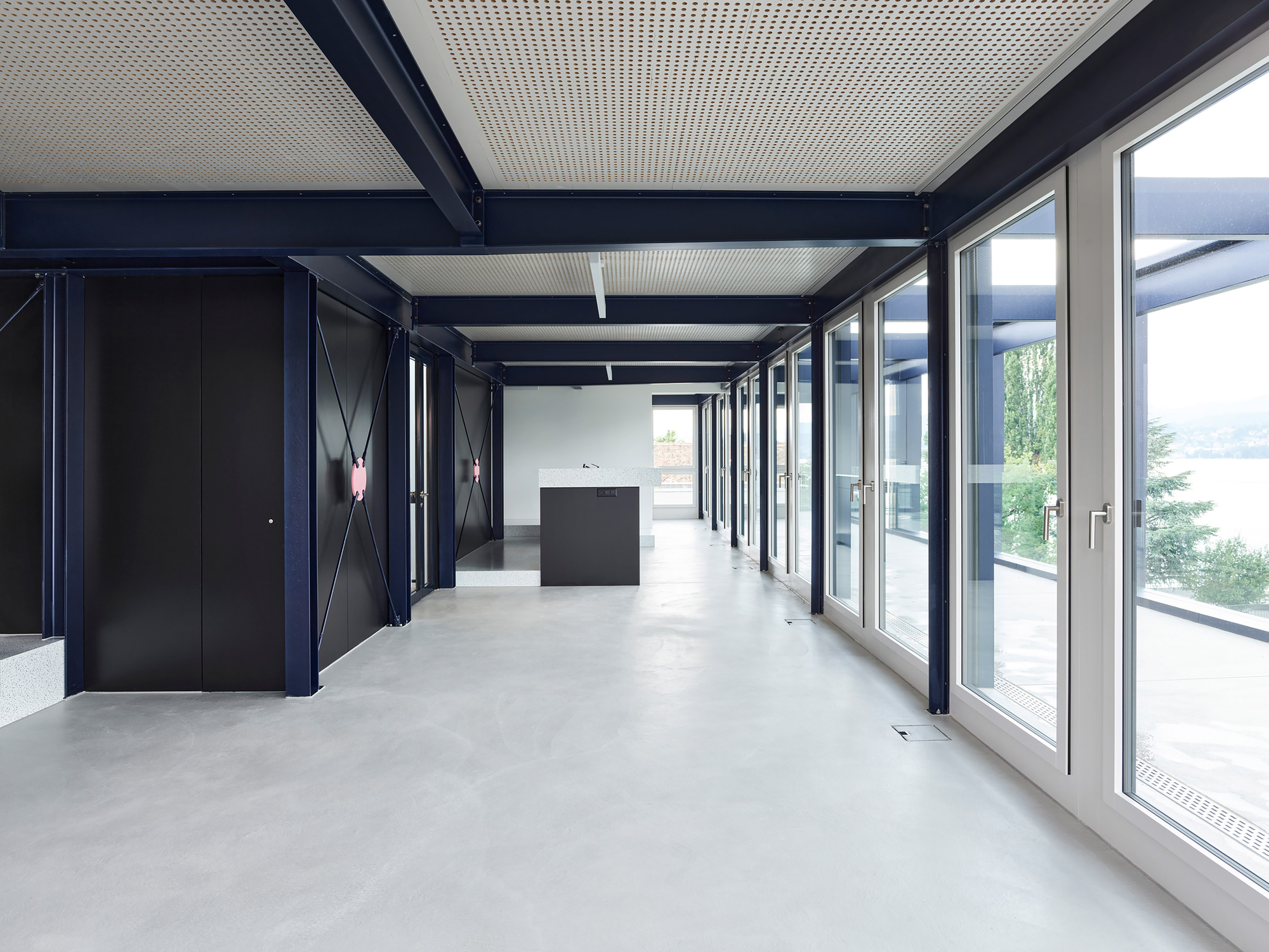 Corridor with floor-to-ceiling glazing, exposed steel beams, and a freestanding dark reception desk