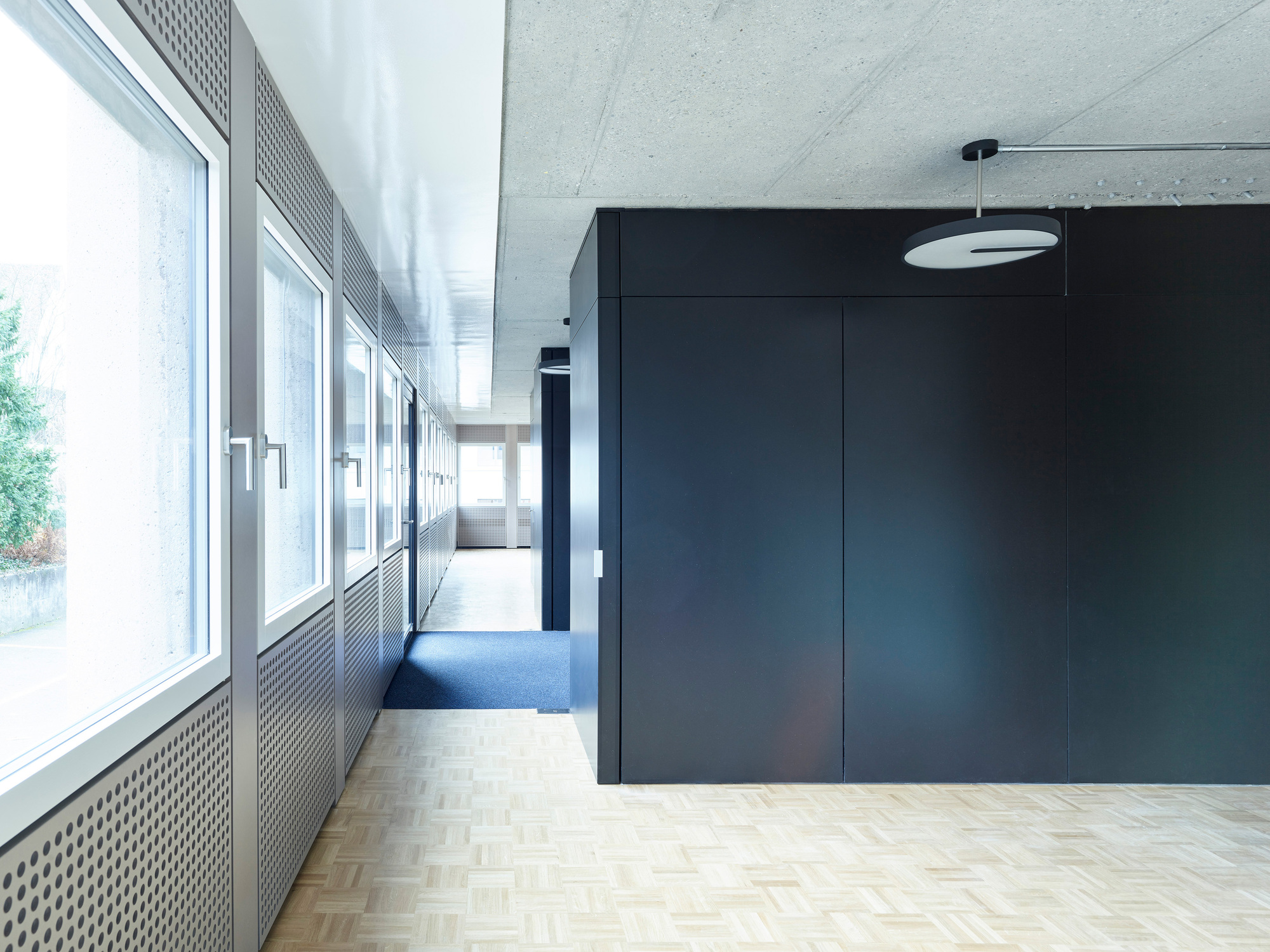 Interior passage with herringbone parquet flooring, metal radiator grilles, and a dark panel wall
