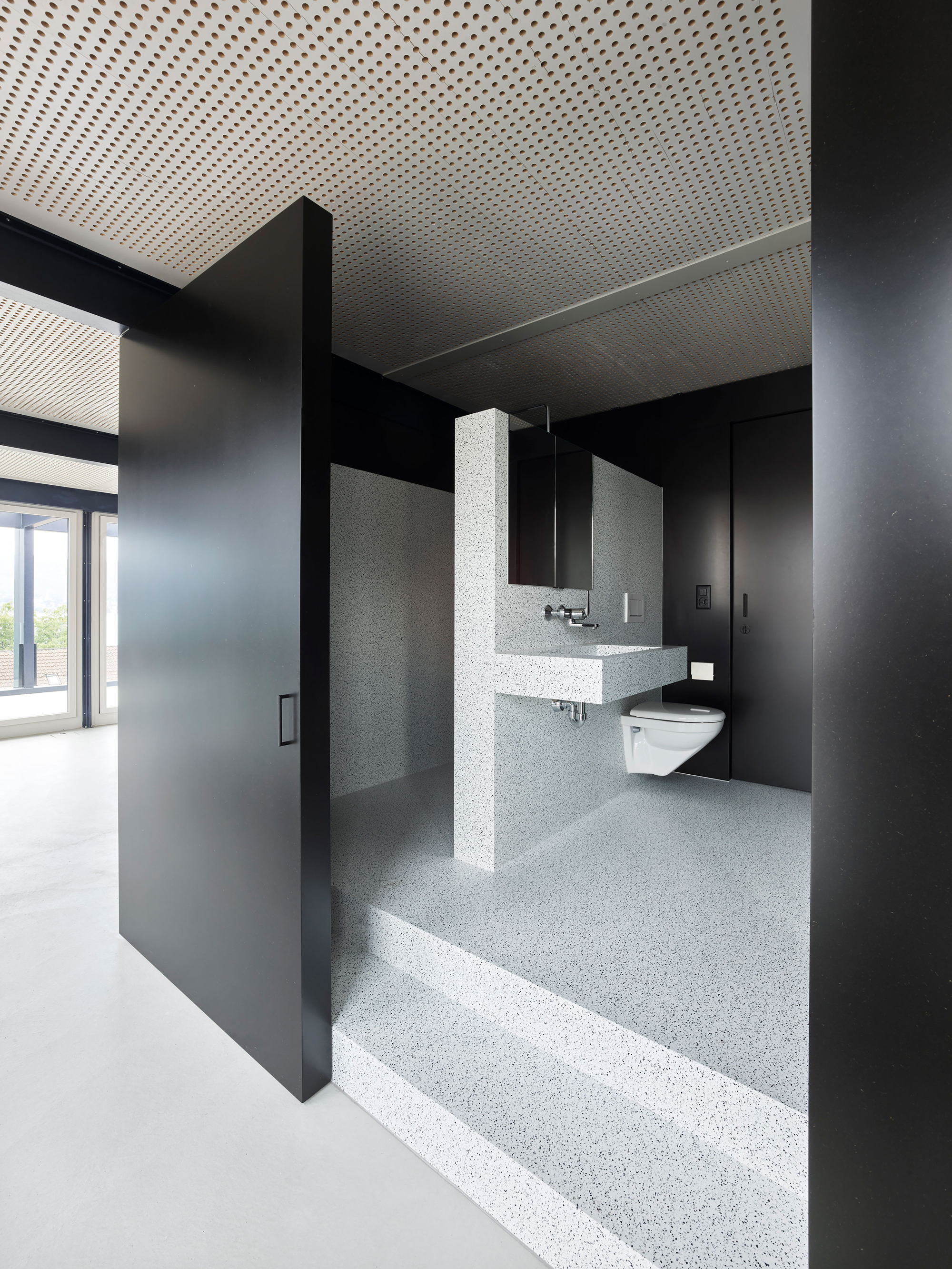 Bathroom with terrazzo flooring, wall-hung sink, and dark metal partition framing the entrance