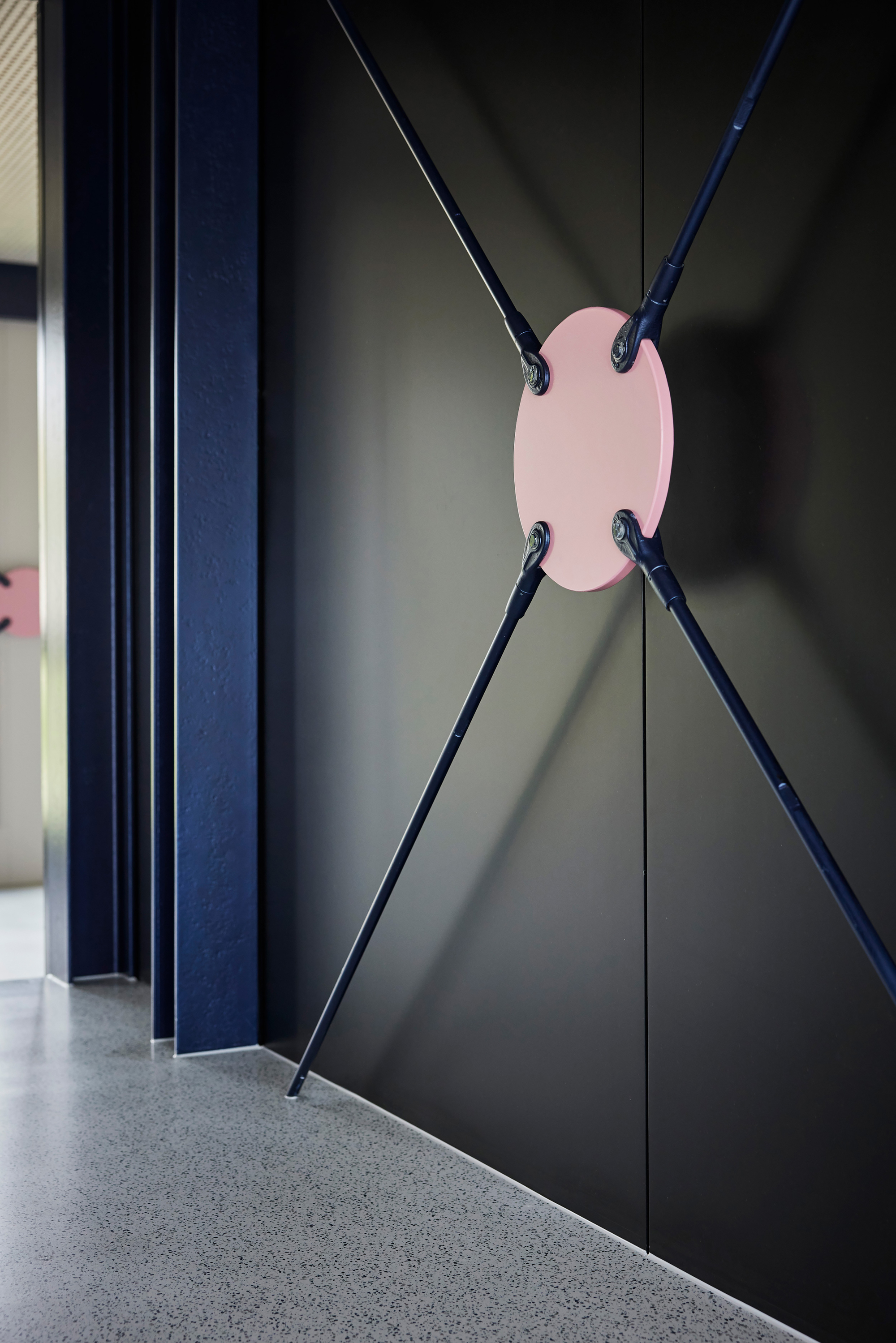 Detail of cable-braced dark metal partition with pink center plate connecting diagonal steel rods