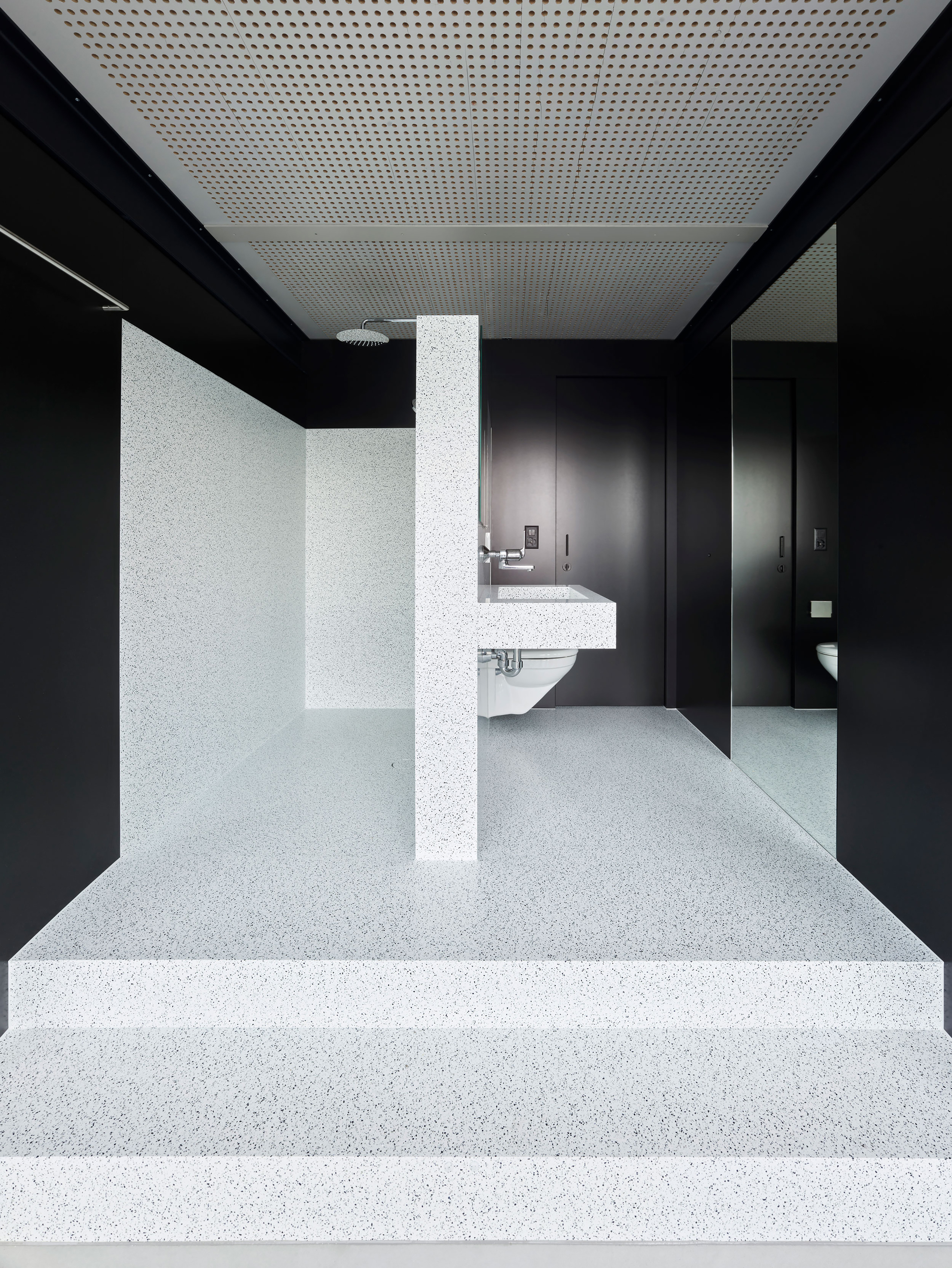 Terrazzo steps ascending toward a restroom with black walls and perforated white ceiling panels