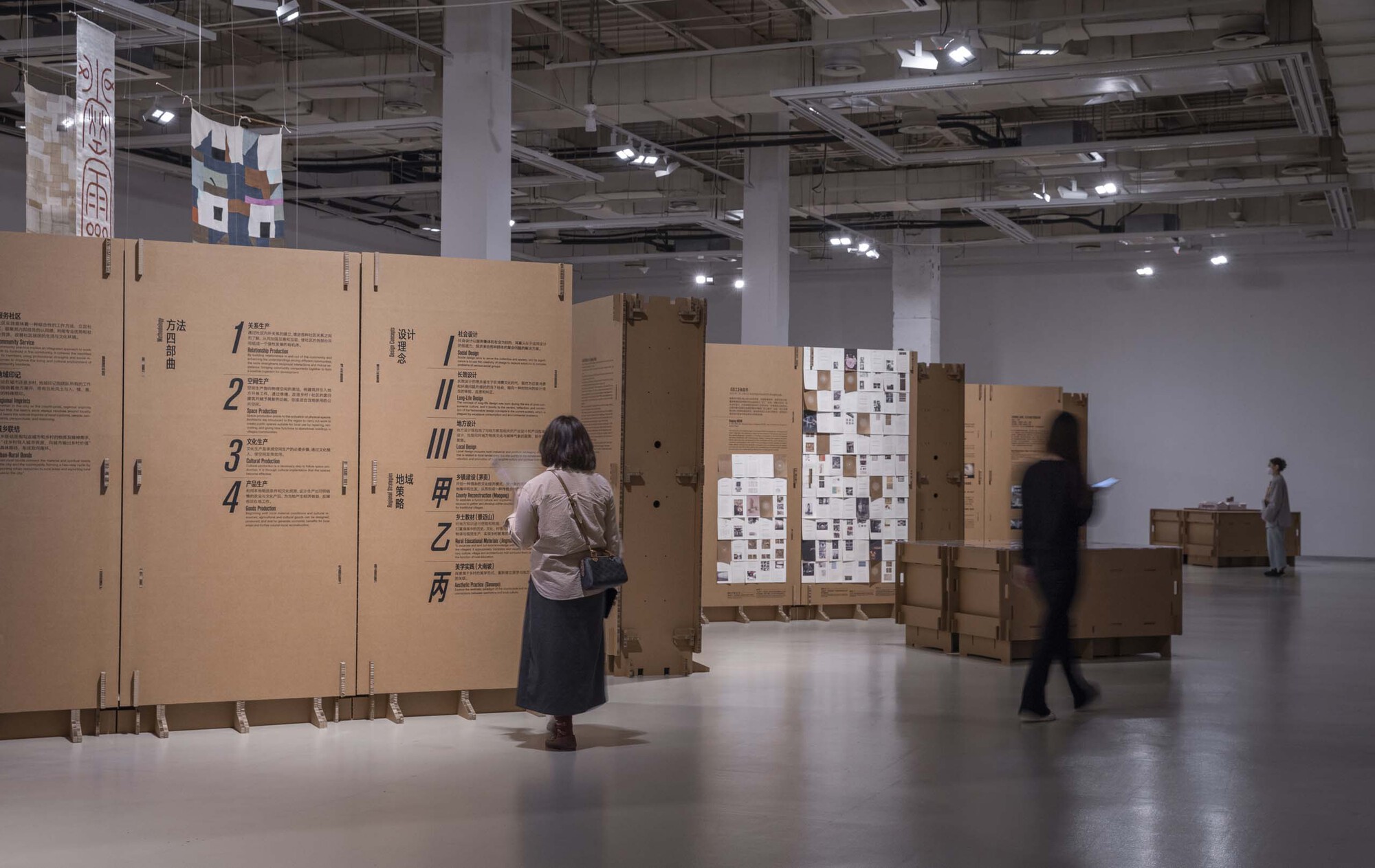 Visitor reading a cardboard information panel as other figures move through the gallery space