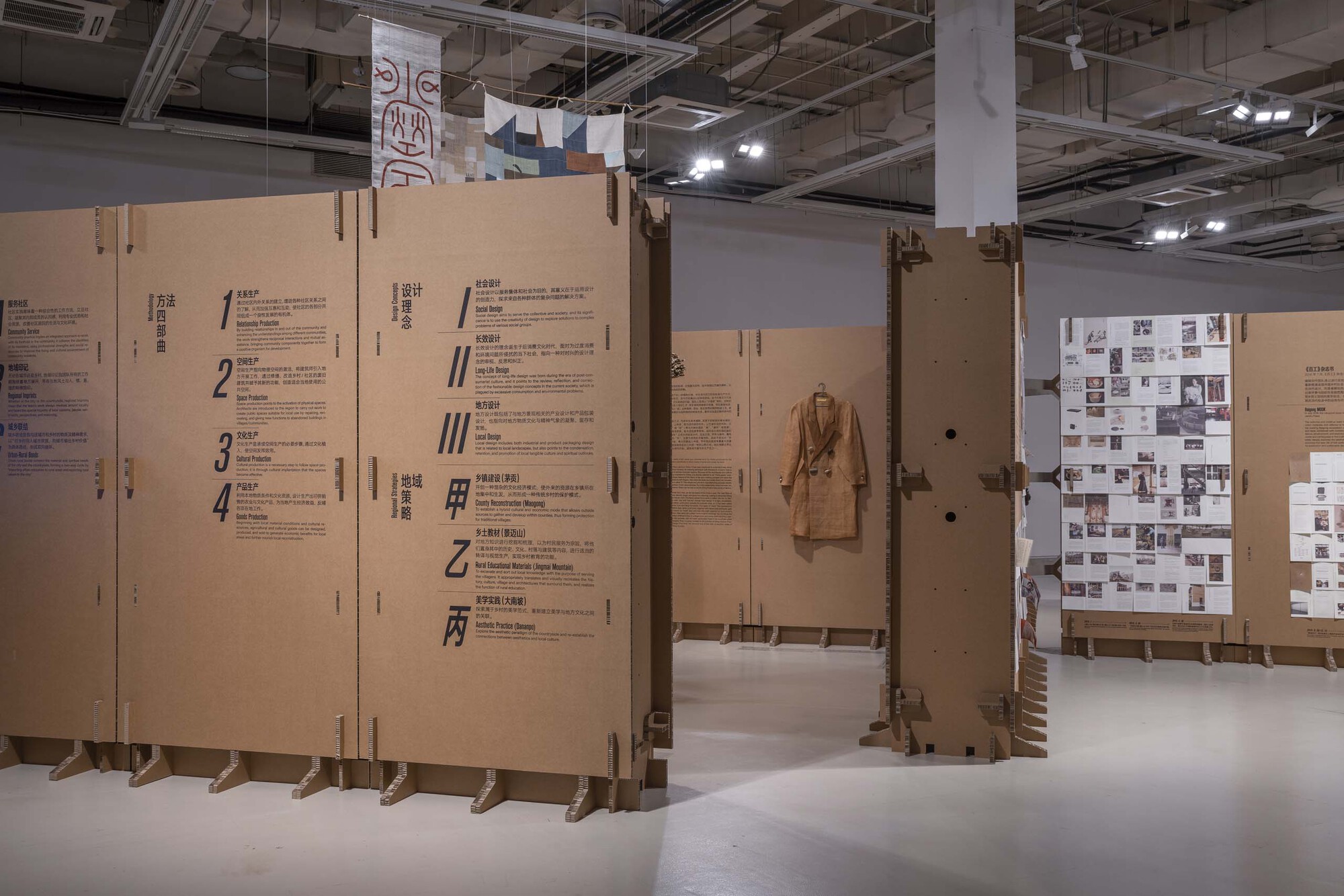 Freestanding cardboard panels with printed text and a hanging garment in a gallery with exposed services