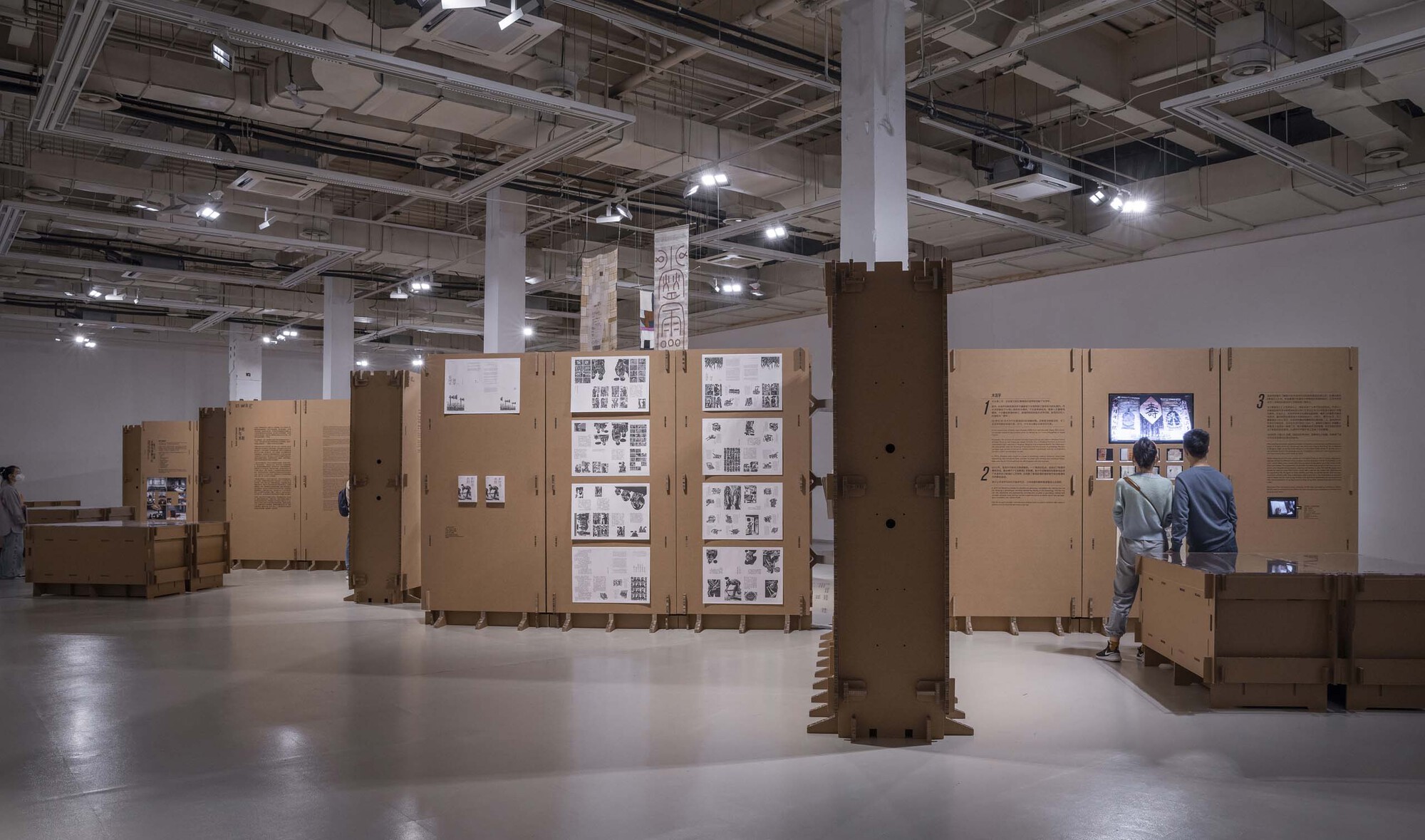 Installation of modular cardboard display systems with video monitors and photograph grids throughout the open hall