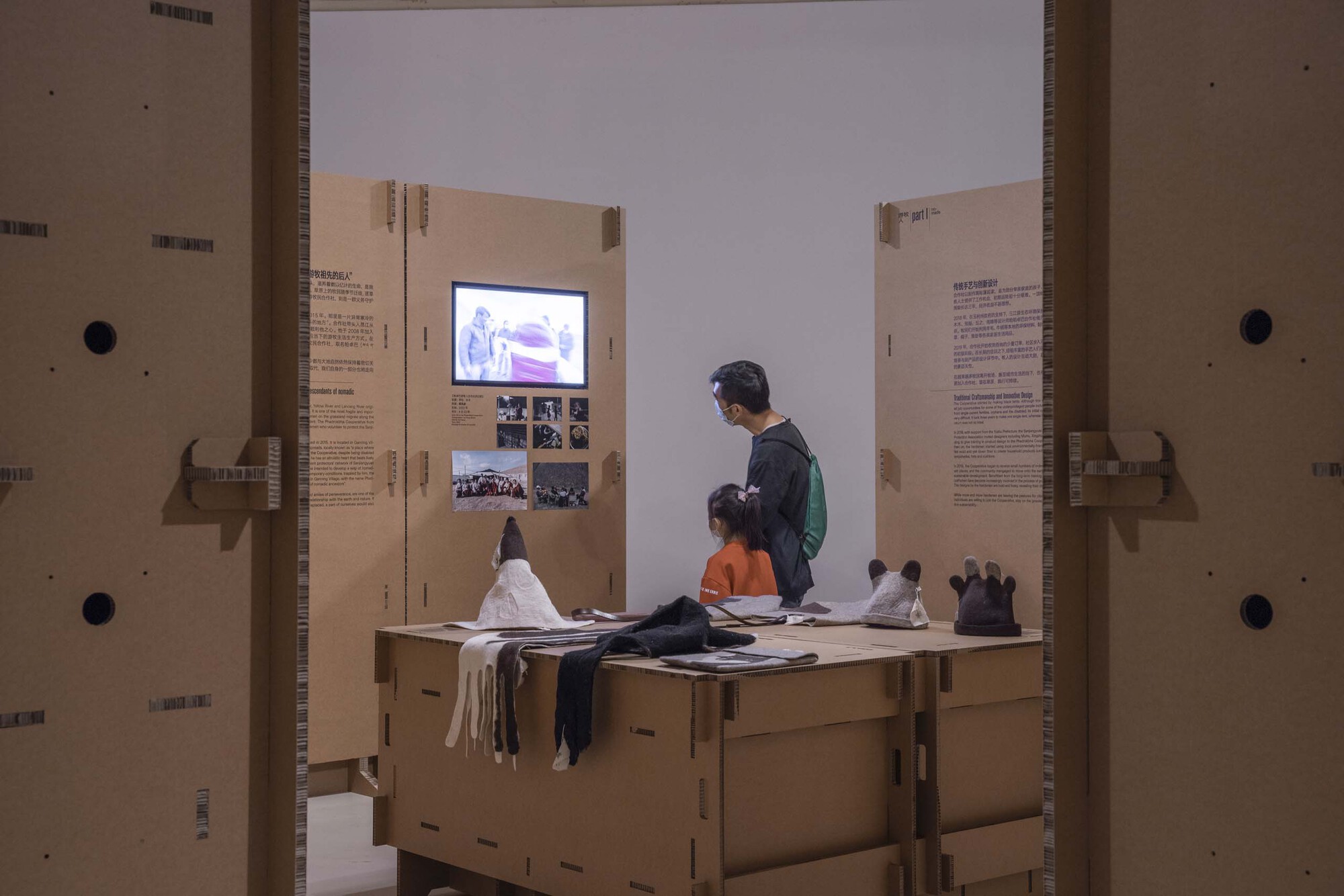 Two visitors seated on a cardboard bench viewing a video monitor between flanking text panels