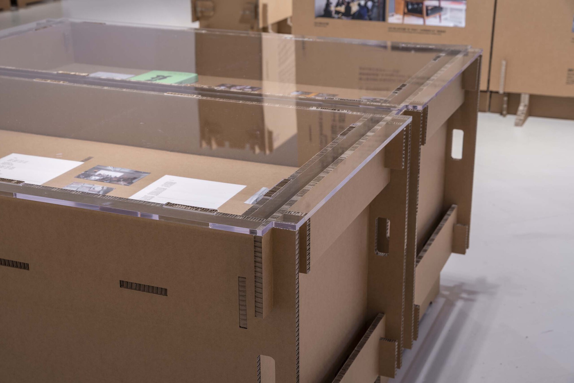 Acrylic-topped cardboard model on a white floor beneath overhead gallery lighting