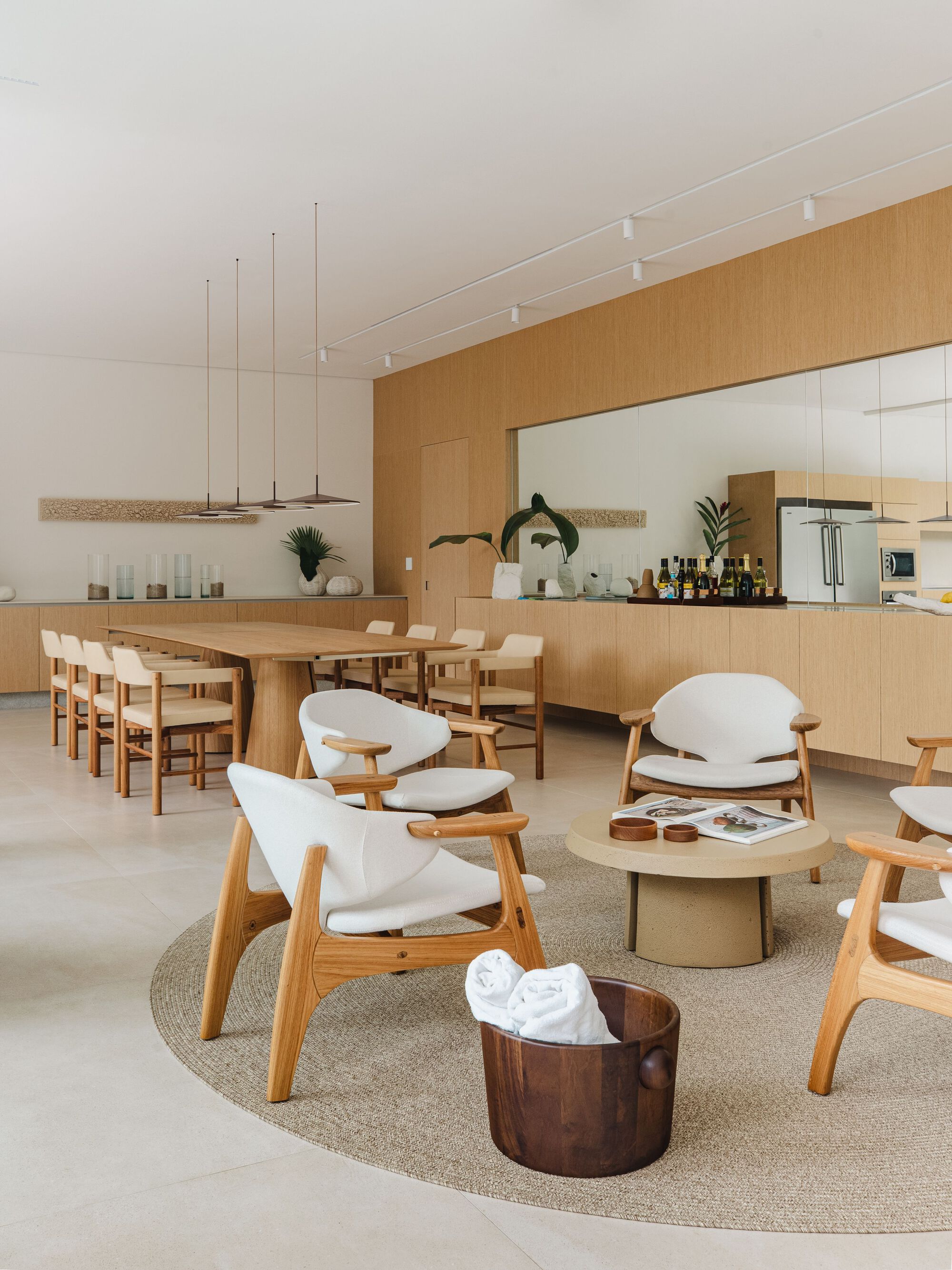 Combined kitchen and dining space with timber cabinetry and mirrored backsplash under linear pendant fixtures