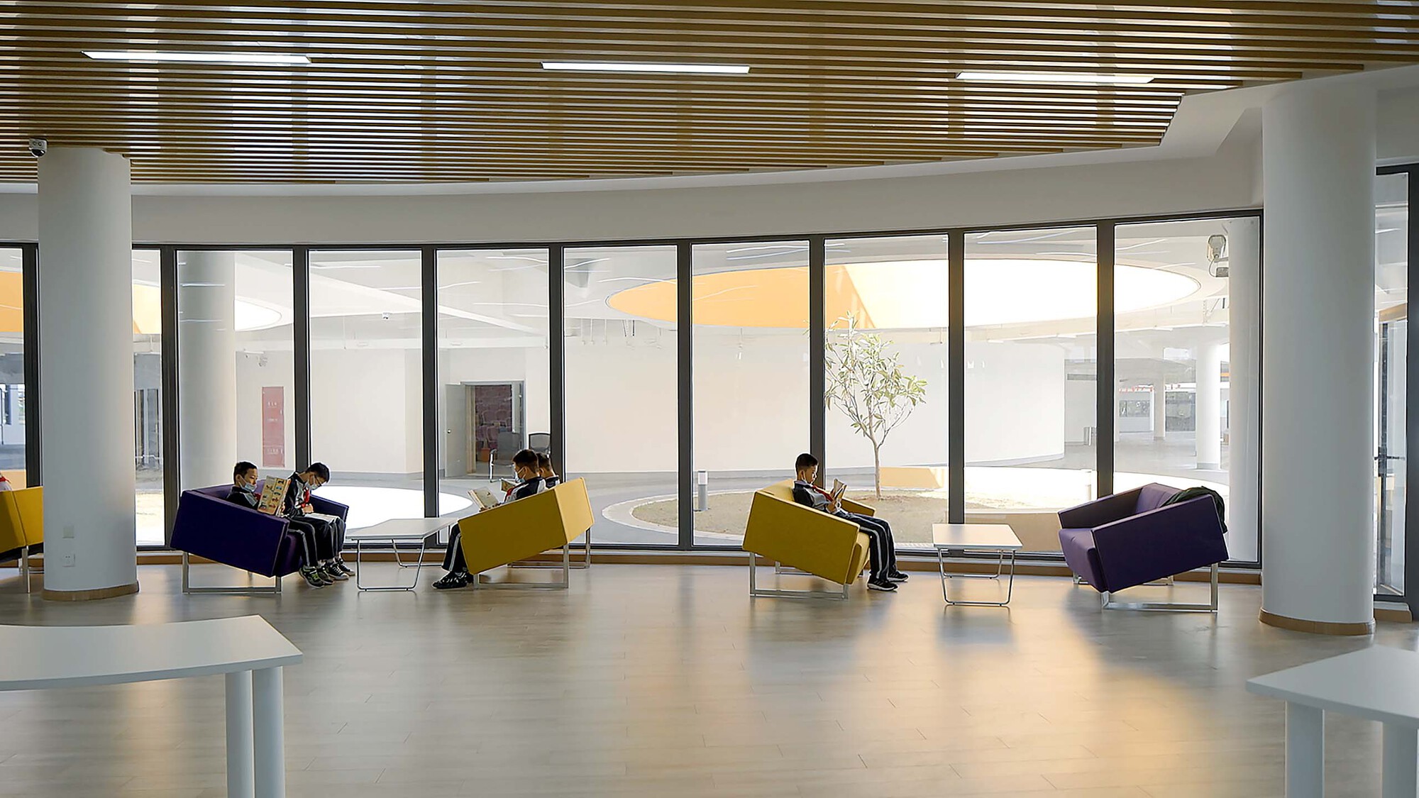 Interior lounge with timber slatted ceiling, white columns, and students seated in yellow and purple chairs