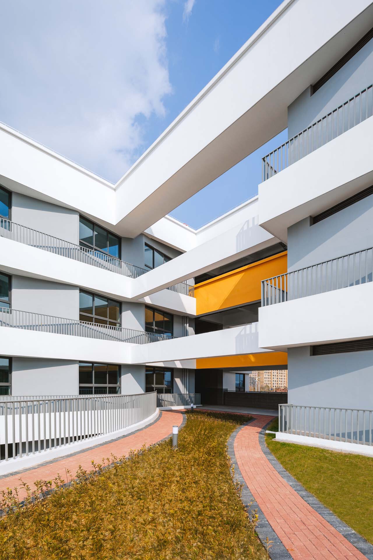 Courtyard view with curved paving paths through planted beds beneath stacked balconies and orange canopies