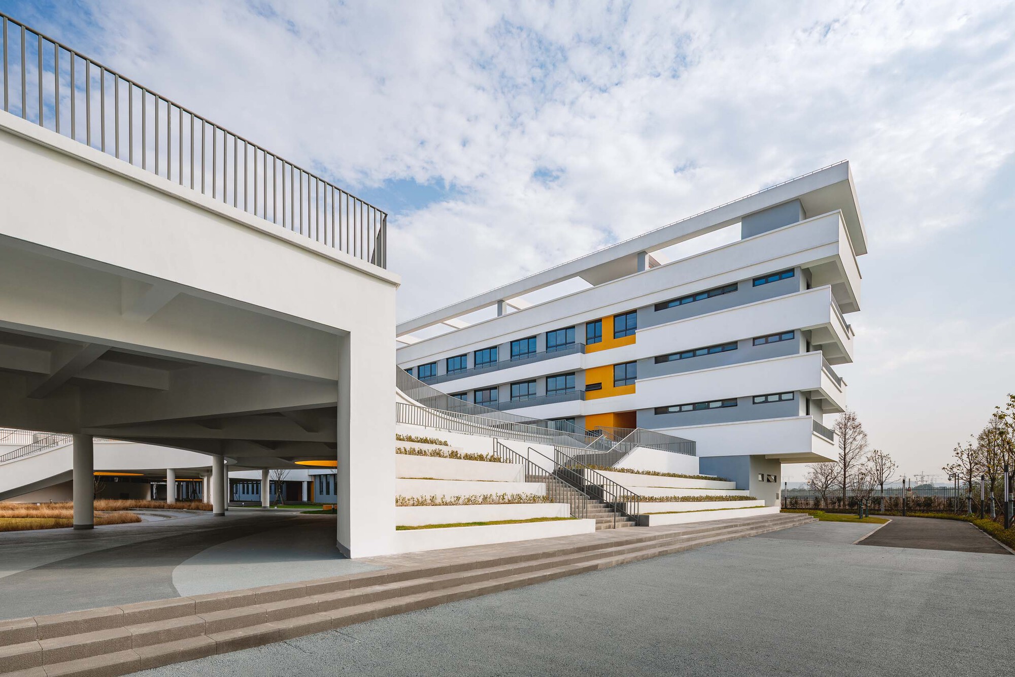 Wide steps descending from a covered entry to a multi-level horizontal facade under cloudy skies
