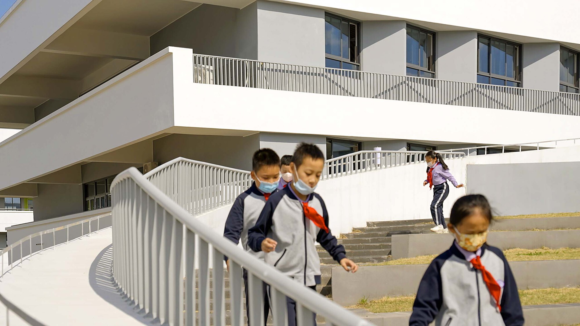 Students with backpacks descending curved outdoor stairs with white metal railings in afternoon light