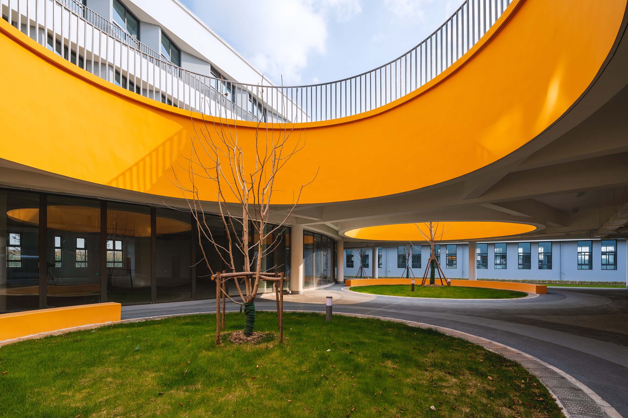 Curved orange canopy sheltering a courtyard with a bare tree and lawn under grey skies