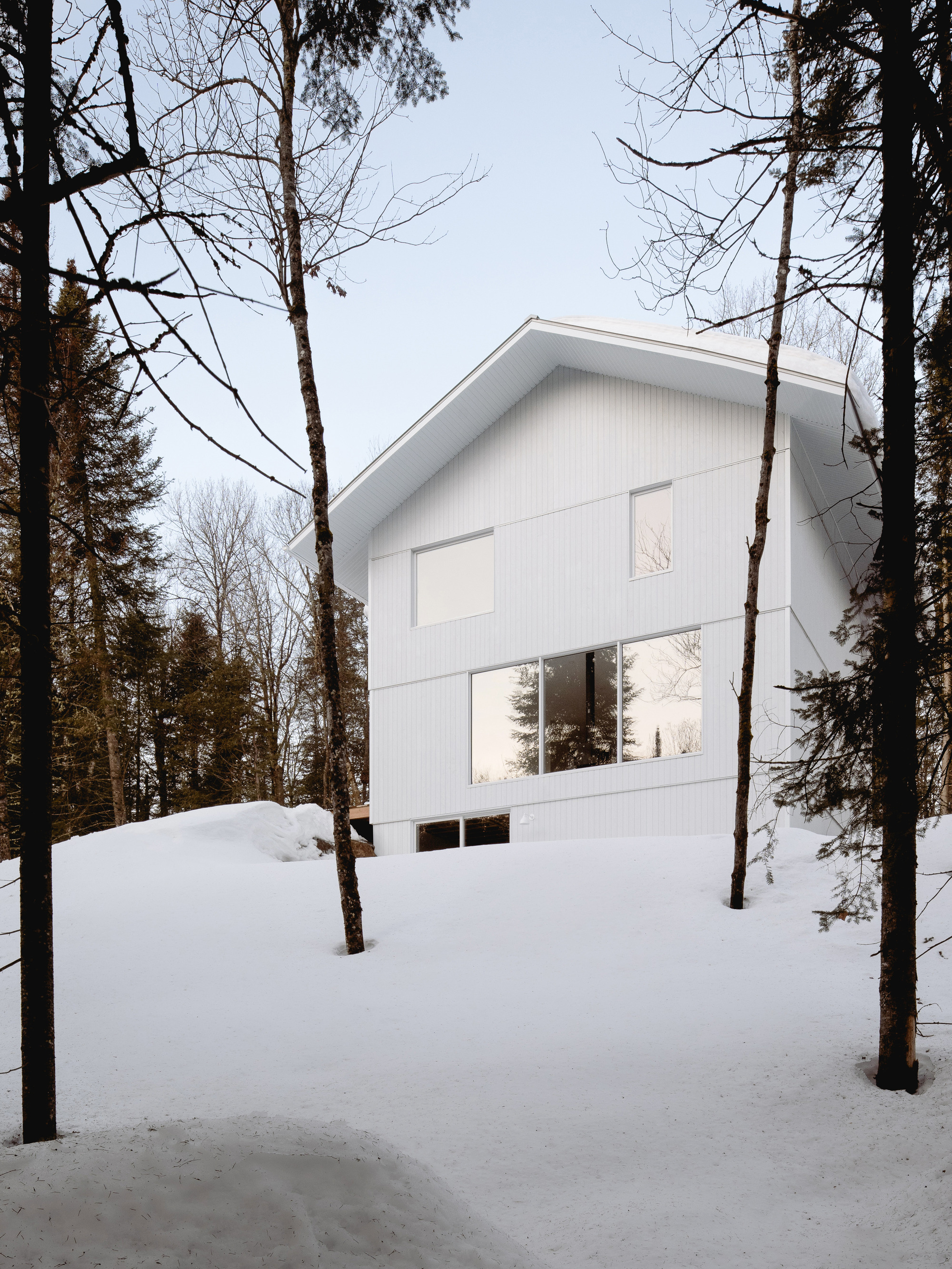 Front elevation showing the gabled volume with large glazing and winter light filtering through bare trees