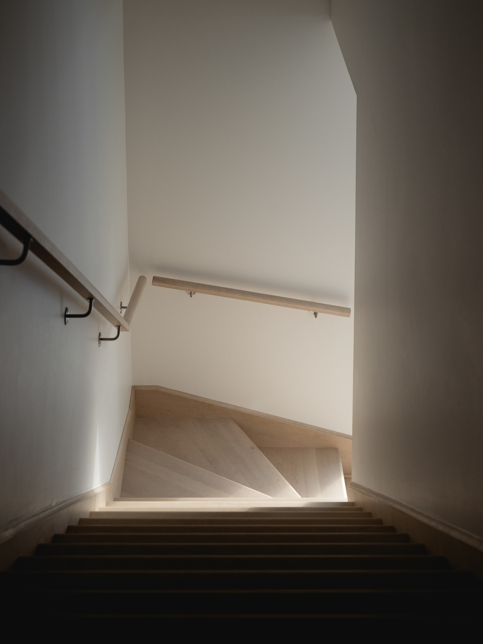 Descending view of a timber staircase with steel handrail brackets and white walls
