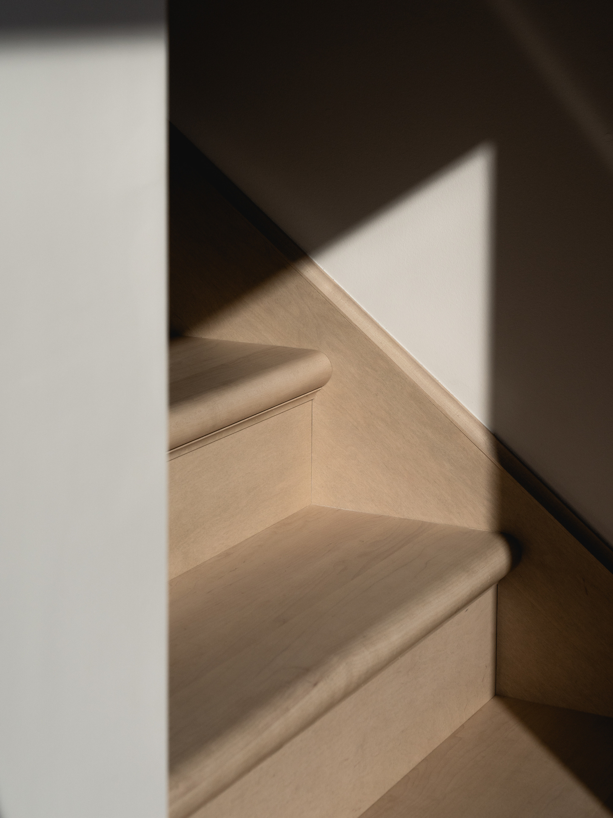 Light wood staircase with black metal handrail and white walls casting triangular shadows