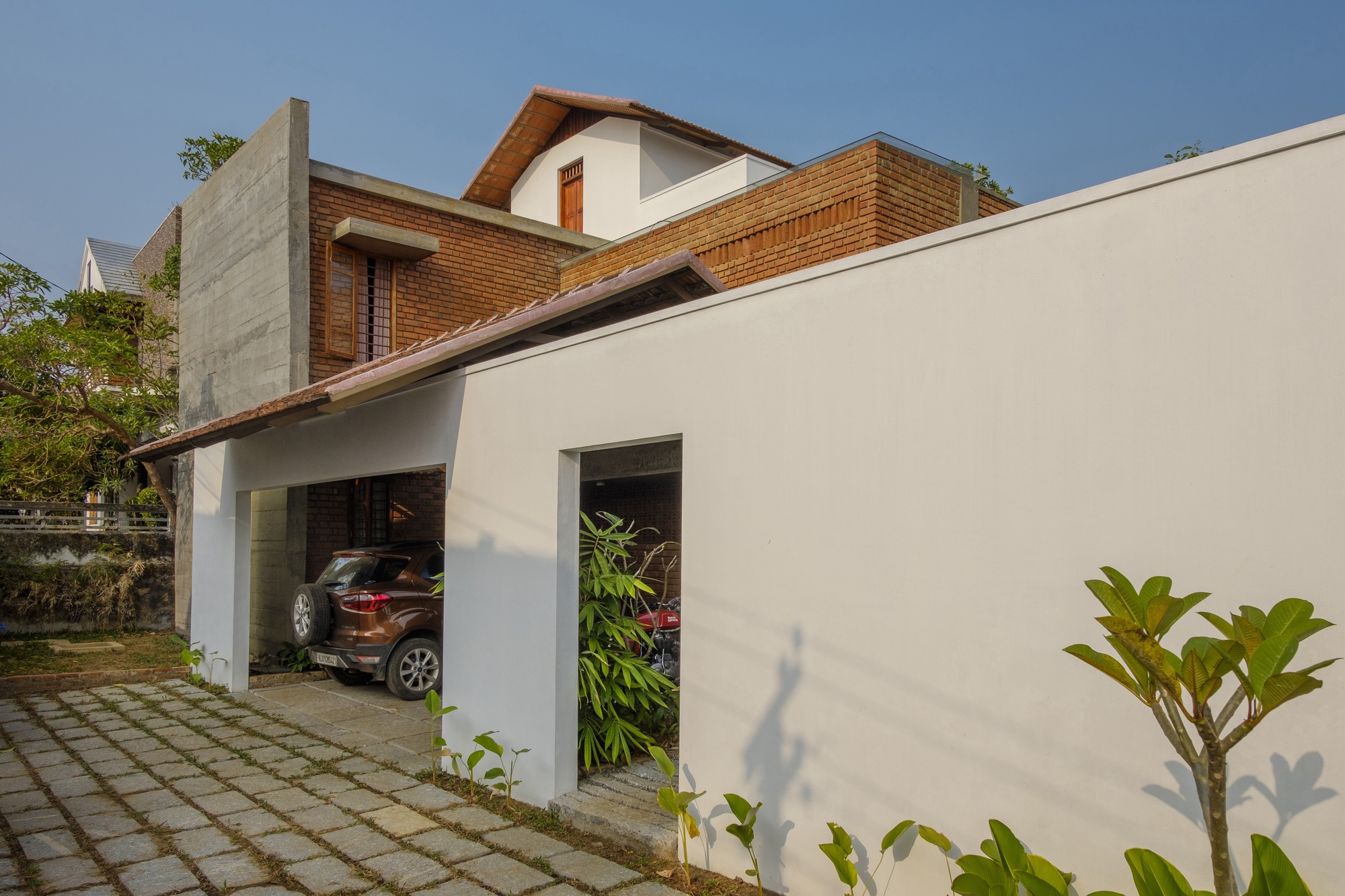 White plastered garage wall with gridded paving and young plantings along the entrance path