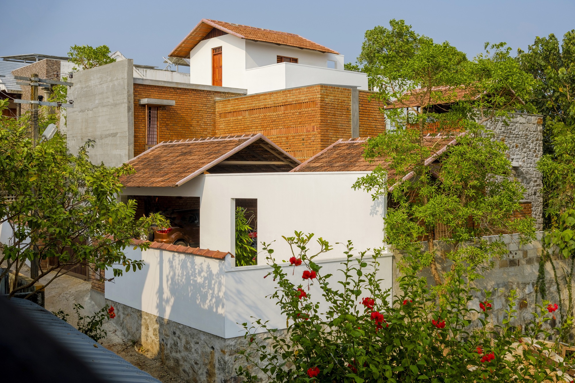 Street view of the stacked volumes and gabled roofs surrounded by flowering roses