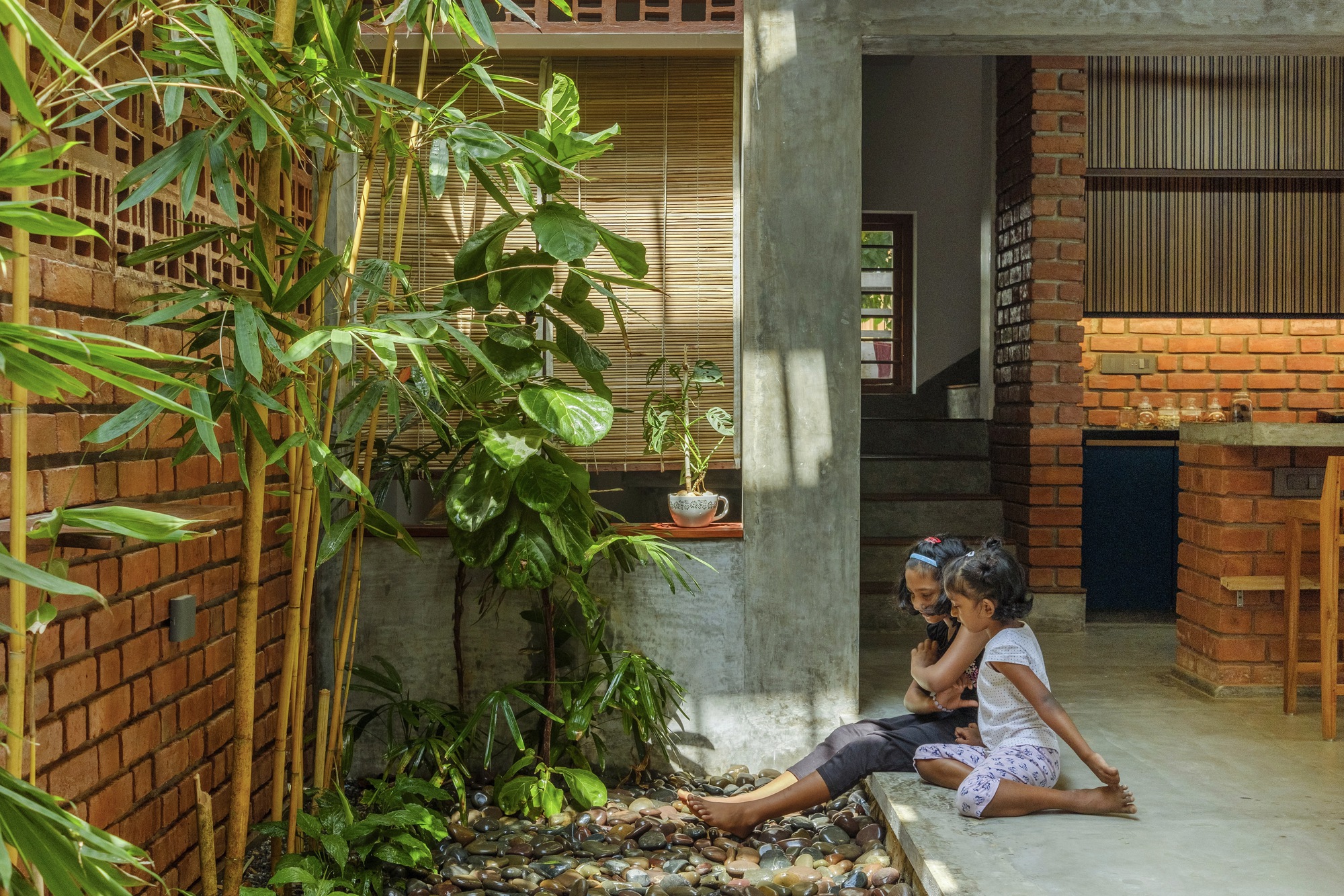 Interior courtyard with concrete columns, exposed brick walls and two children seated by planted greenery