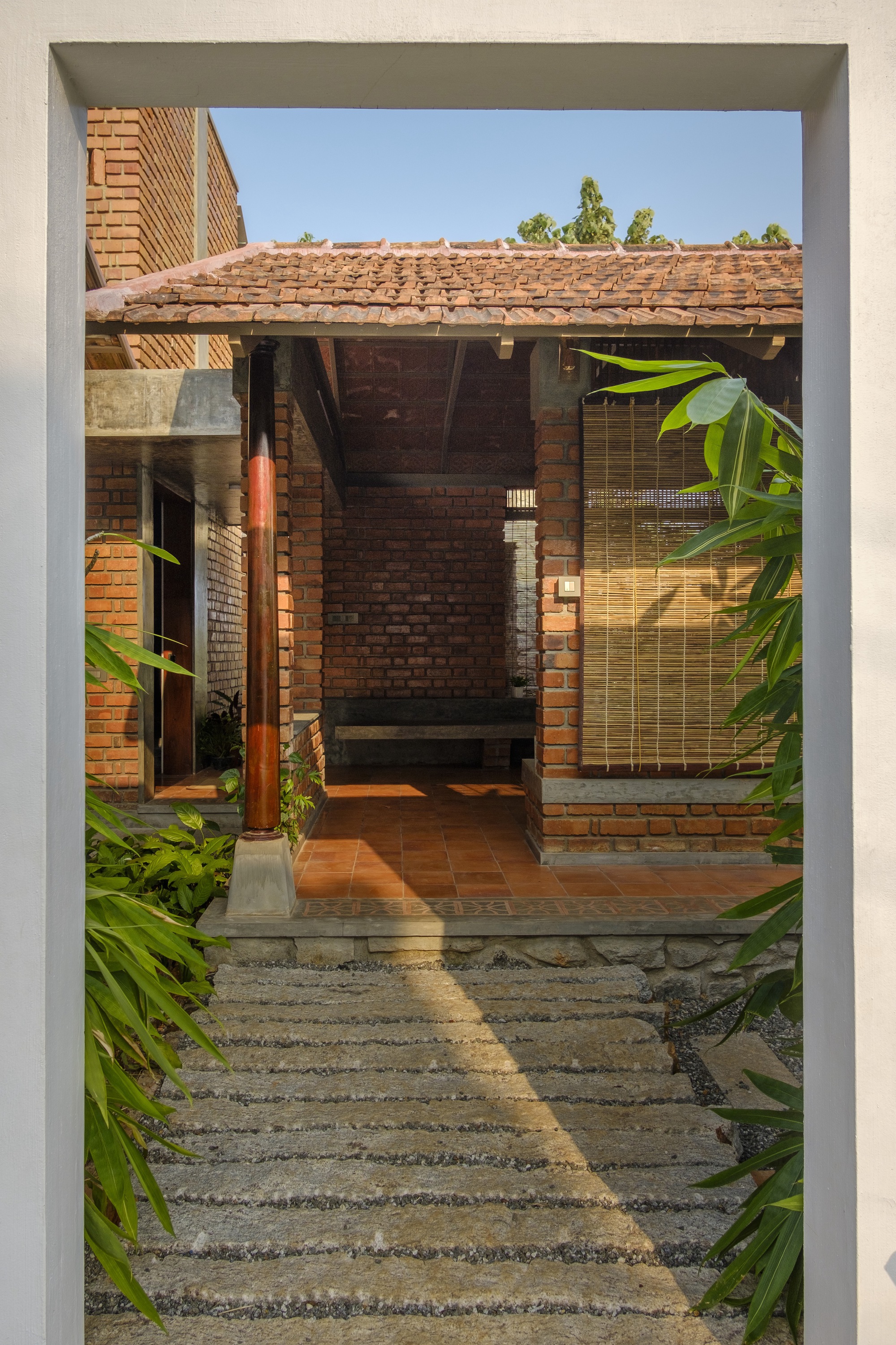 View through doorway to covered terrace with clay tile floor and bamboo screen in afternoon light