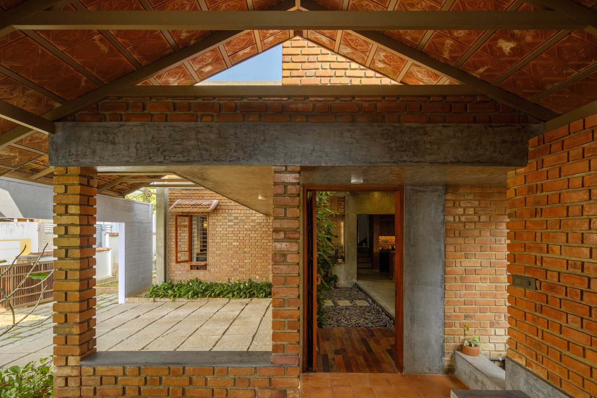 Entry pavilion with exposed timber roof trusses, brick piers and concrete beam framing courtyard beyond
