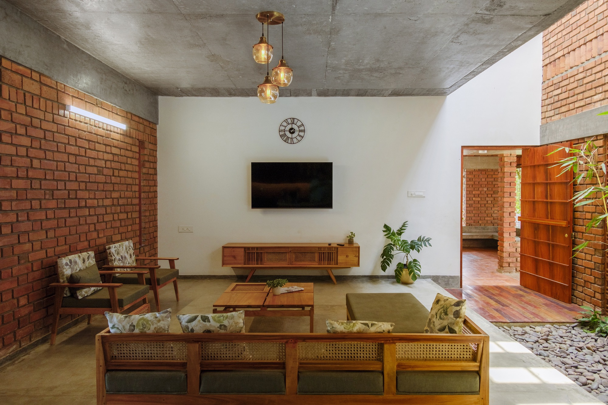 Living room with exposed brick walls, wooden furniture and three brass globe pendants below a concrete vault ceiling
