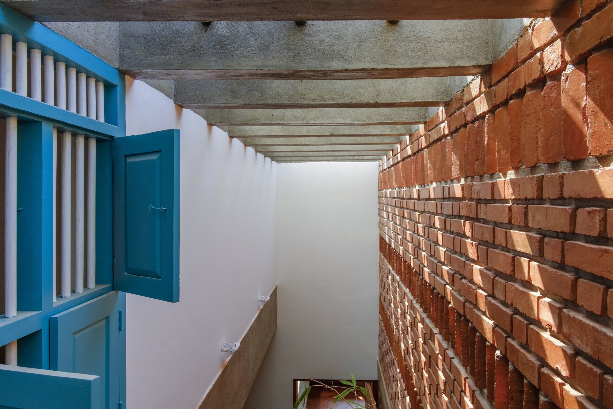 Corridor with exposed brick wall on one side and blue painted timber screen on the other under concrete beams