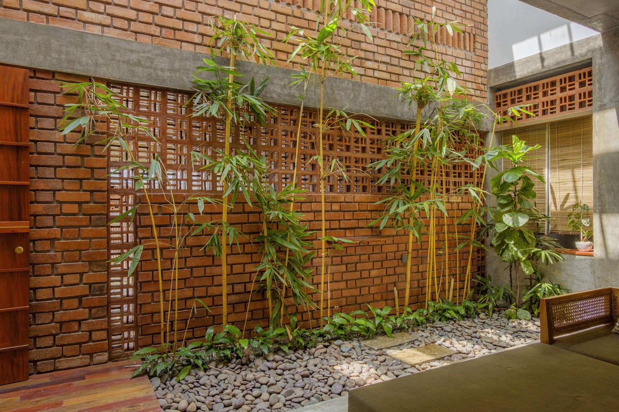 Interior courtyard with bamboo planted in a gravel bed beneath latticed brick screens and exposed concrete beams