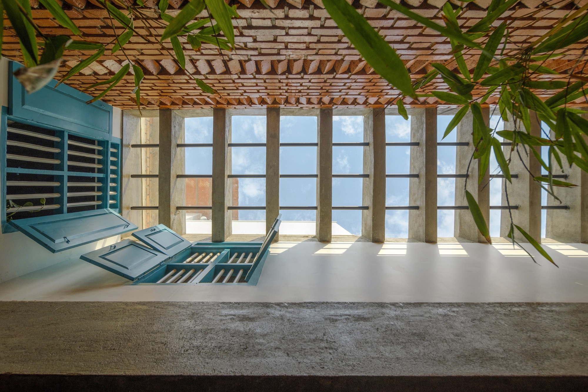 Terrace with blue louvered shutters, bamboo overhead trellis and concrete framed glazing under bright afternoon light