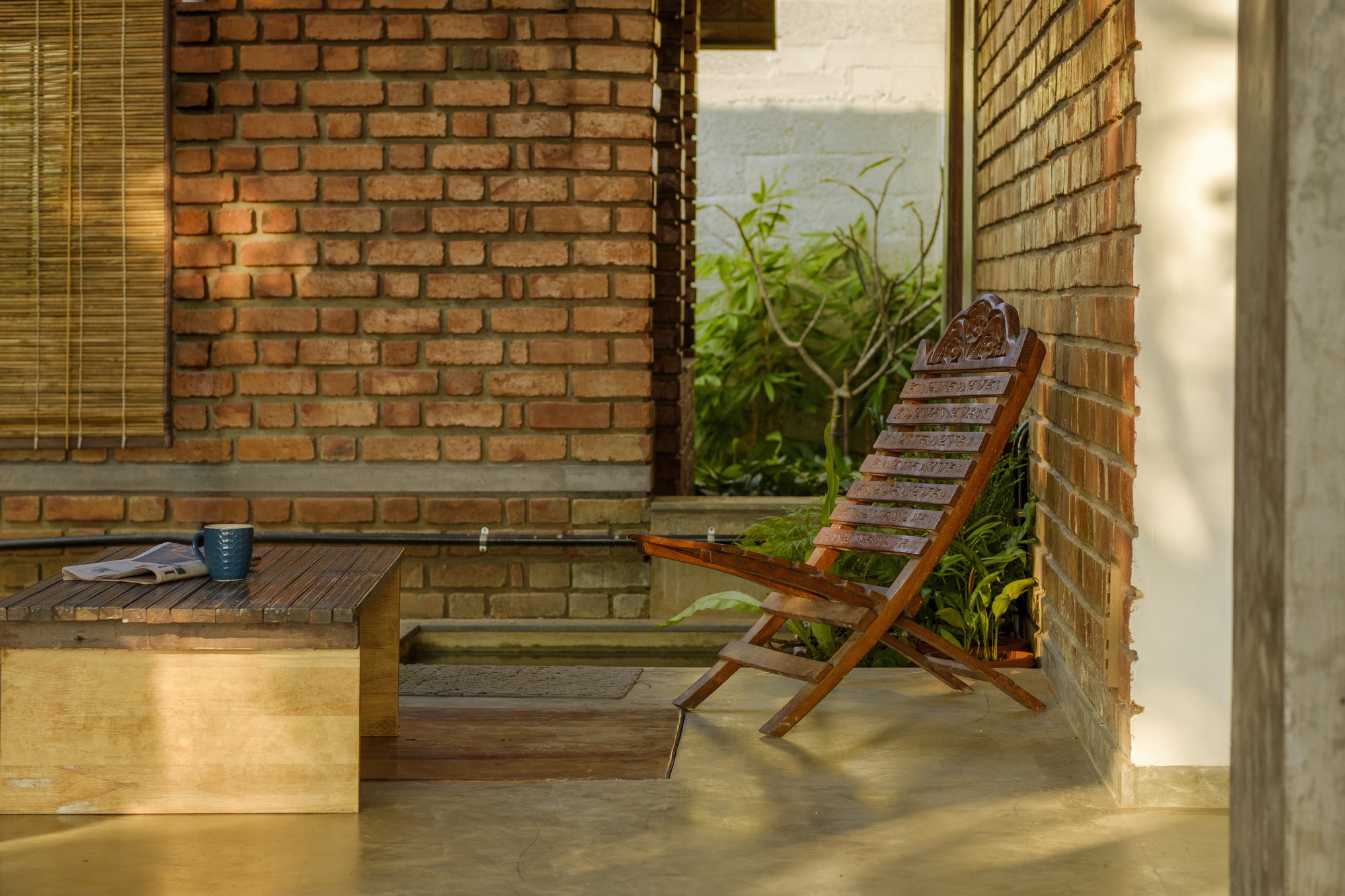 Covered terrace with exposed brick walls, folding wooden chair, and low platform bed in dappled afternoon light
