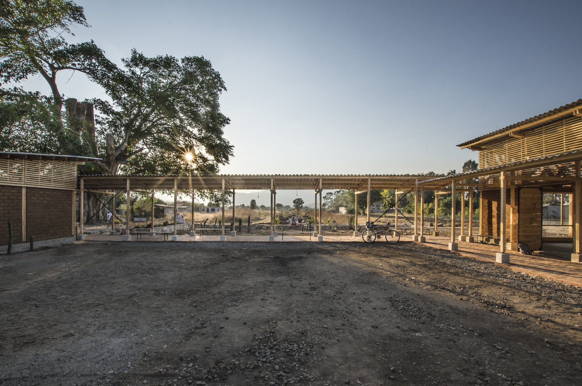 Covered courtyard space with corrugated metal roof and timber columns viewed at dusk with surrounding landscape
