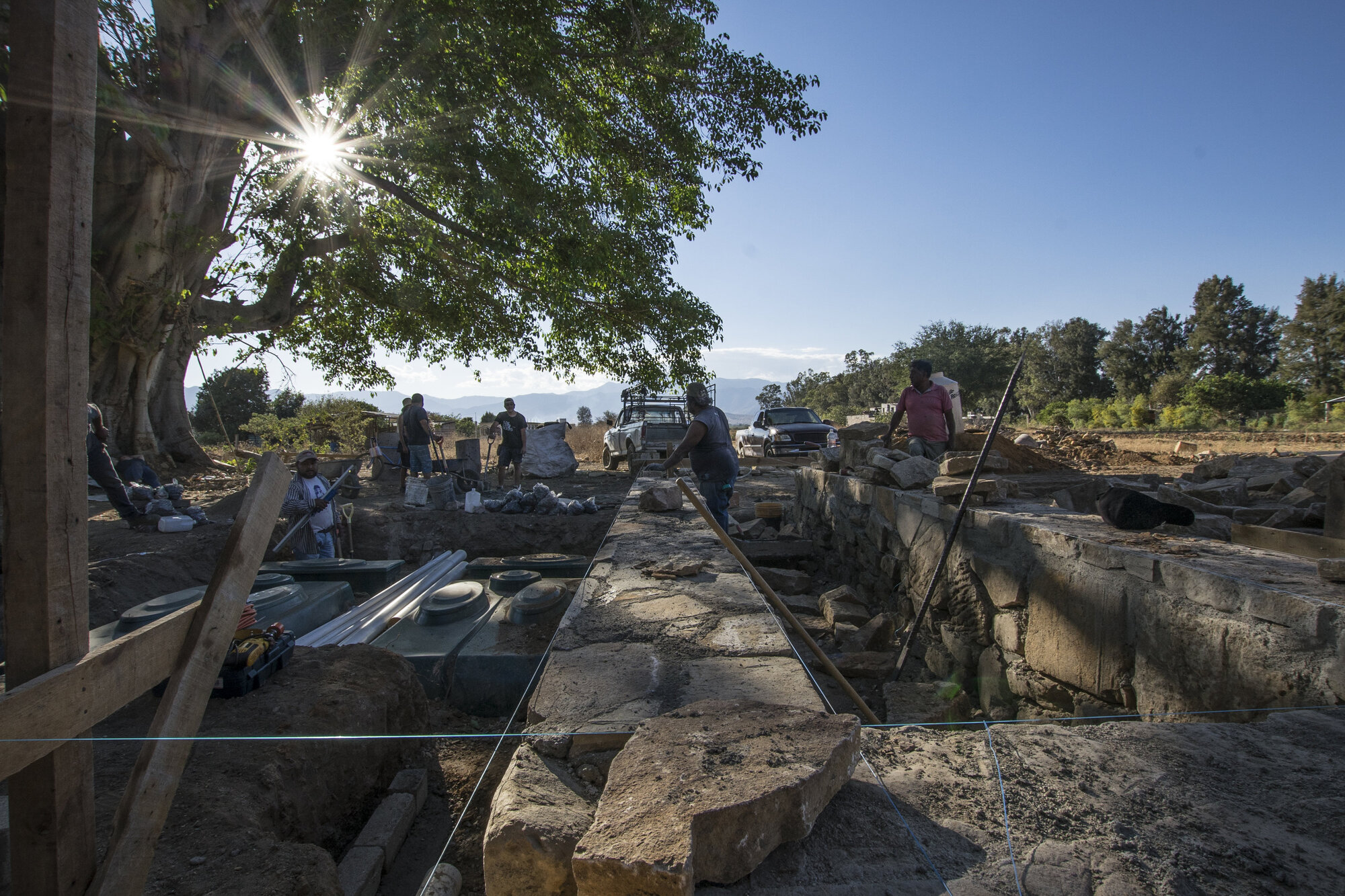 Stone foundation blocks and timber formwork beneath a large tree on the construction site