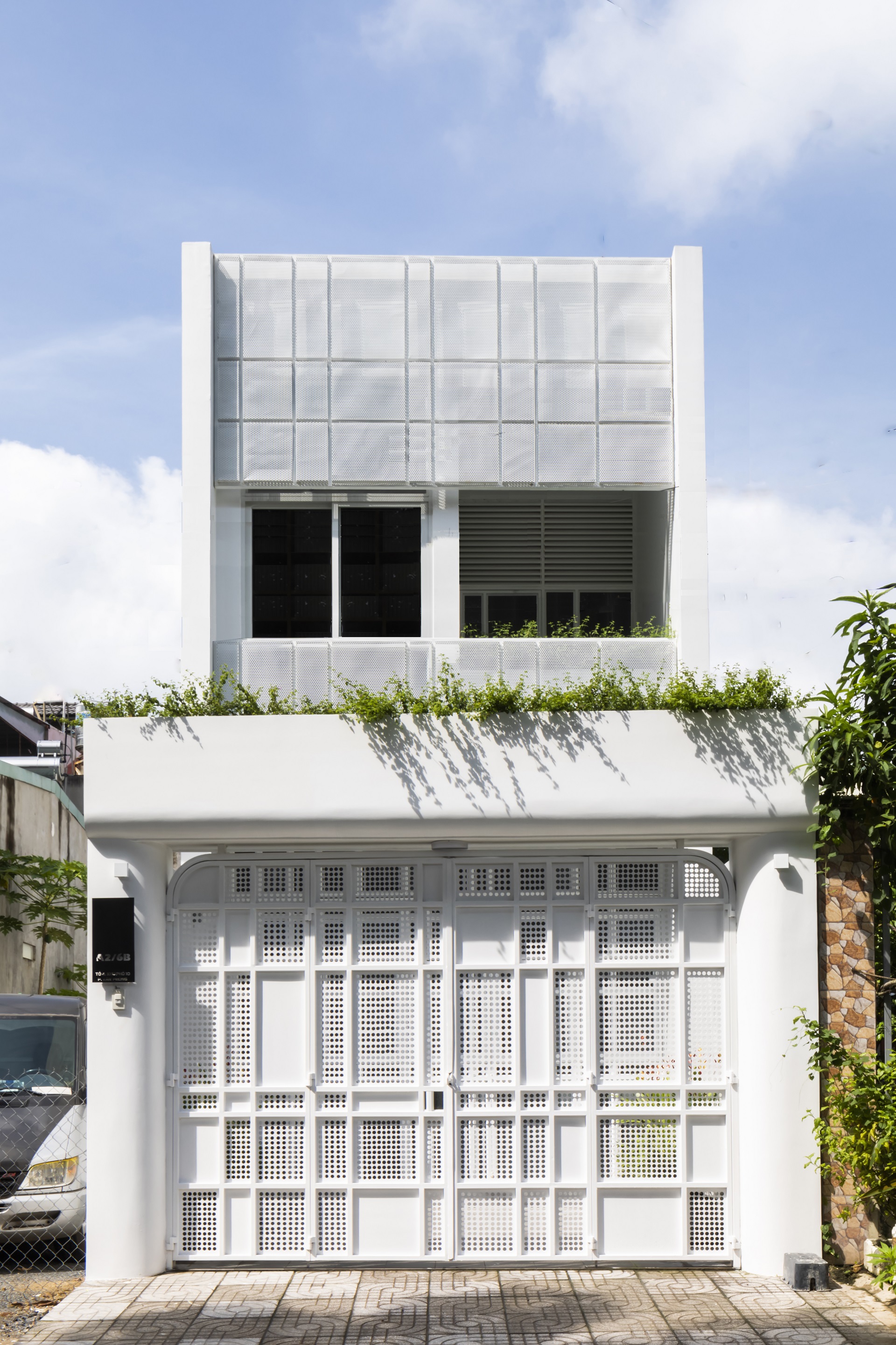 Street-facing facade with white perforated metal gates below a grid of frosted glass panels and planted rooftop