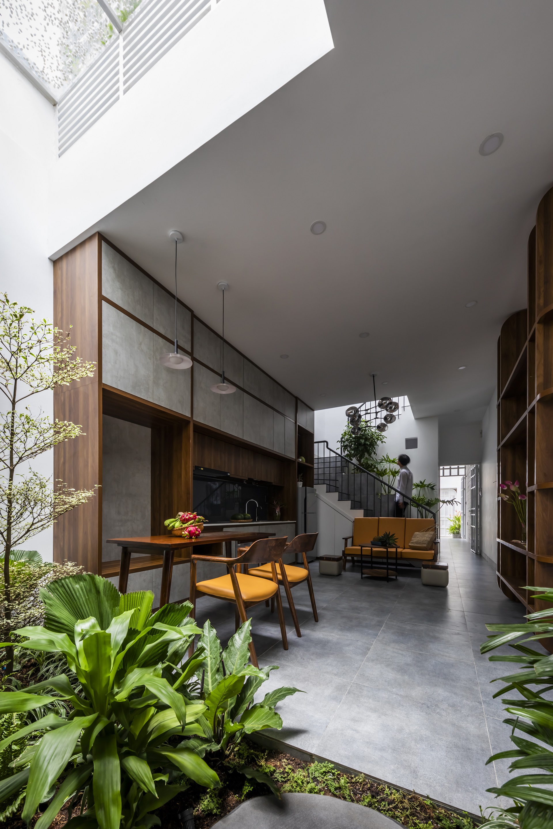 Living and dining area with timber cabinetry opening to an interior planted courtyard under a skylight