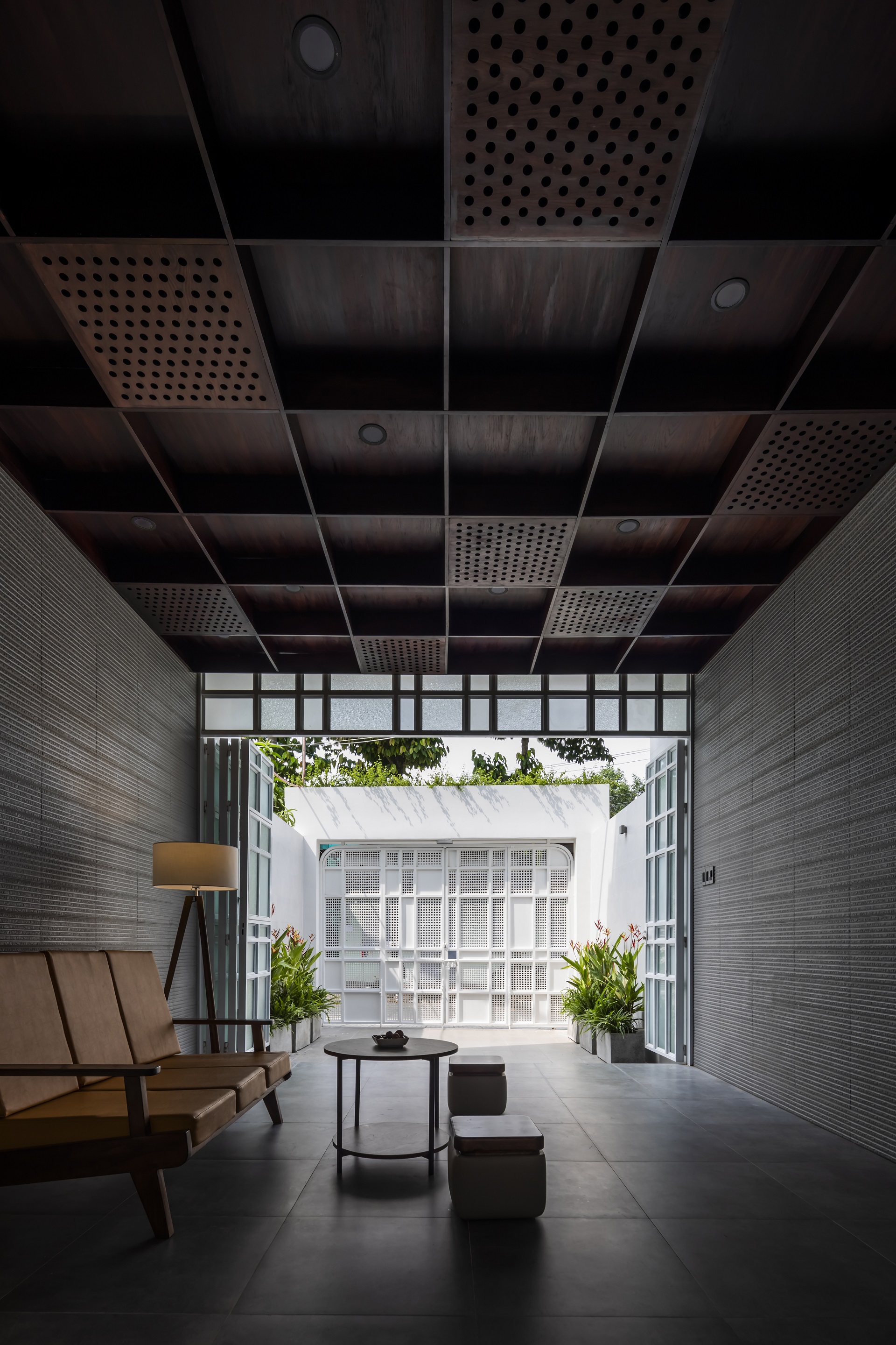 View through perforated ceiling panels toward the white perforated facade framed by textured wall tiles