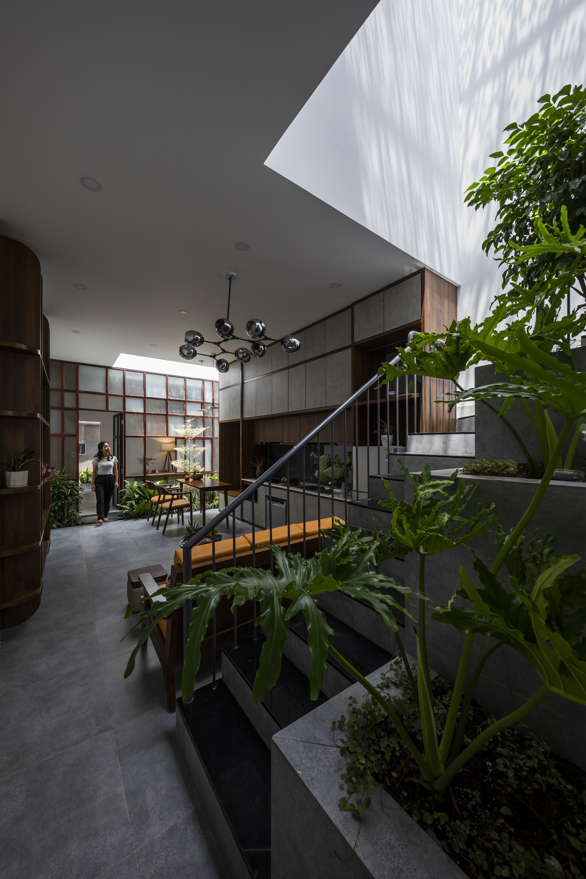 Helical steel staircase winding through planted beds beneath an angular skylight with diffused sunlight