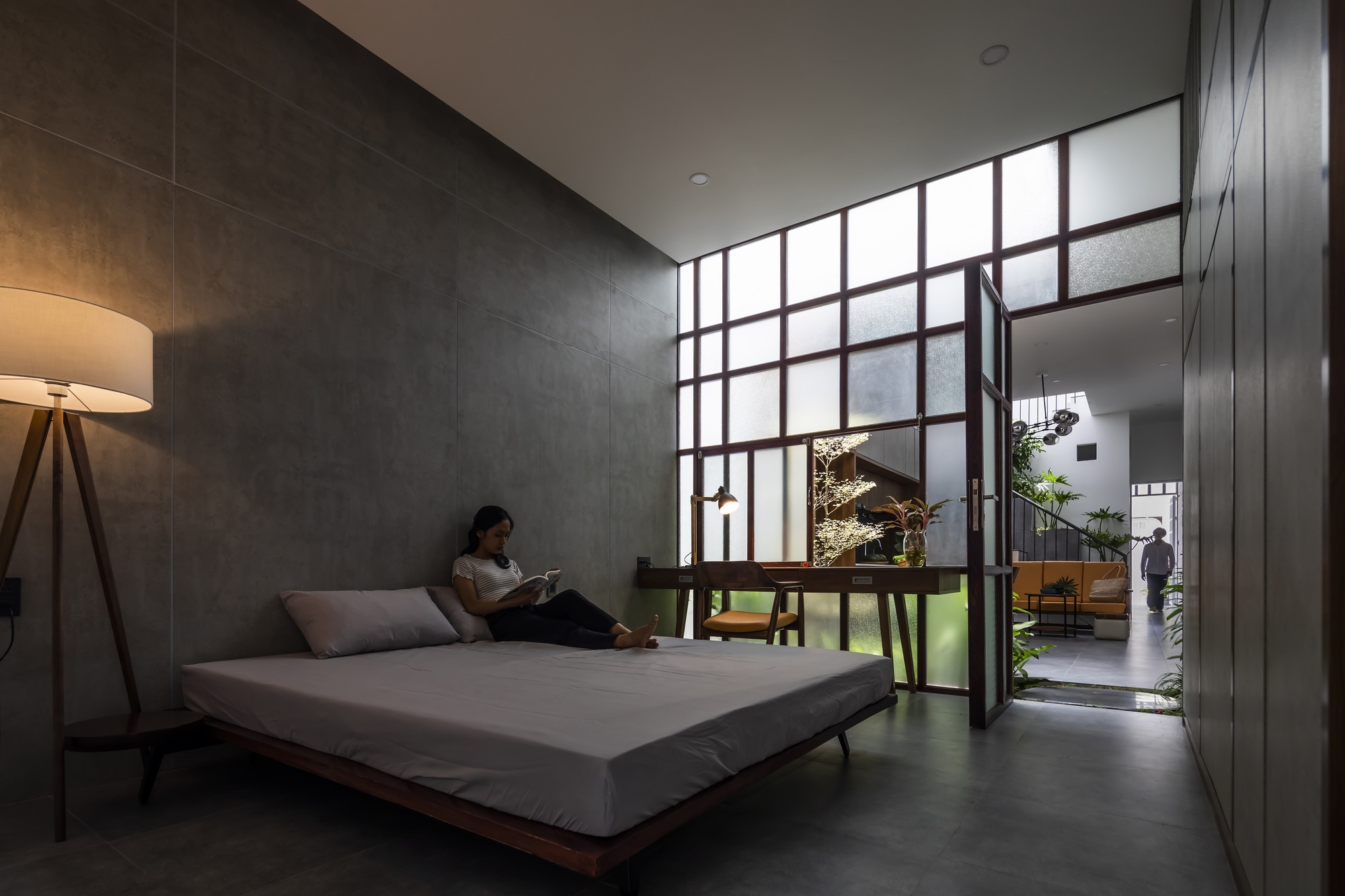 Bedroom with dark tile wall and gridded glass partition opening to an interior courtyard