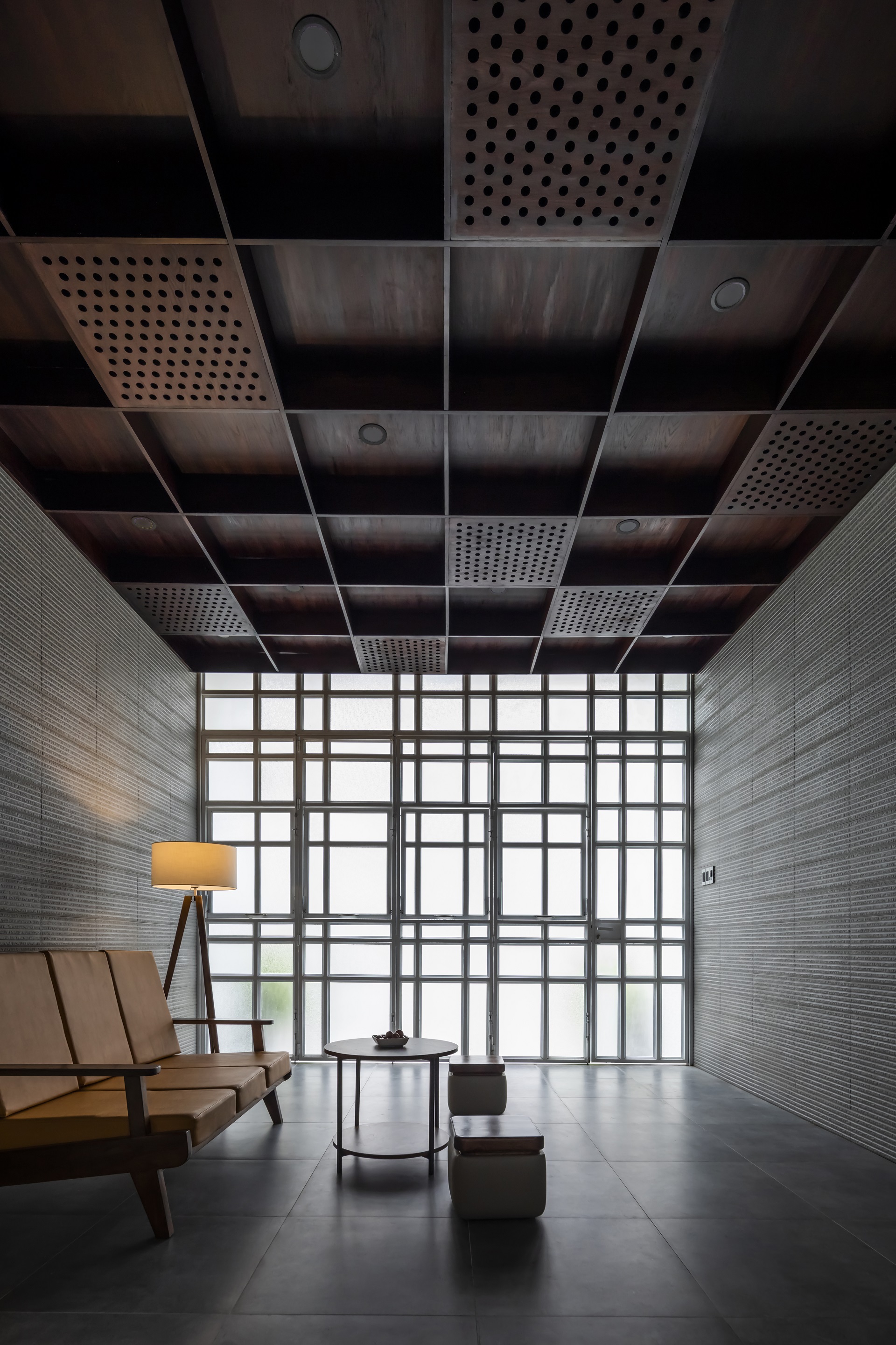 Seating area beneath perforated metal ceiling panels with gridded glass wall beyond