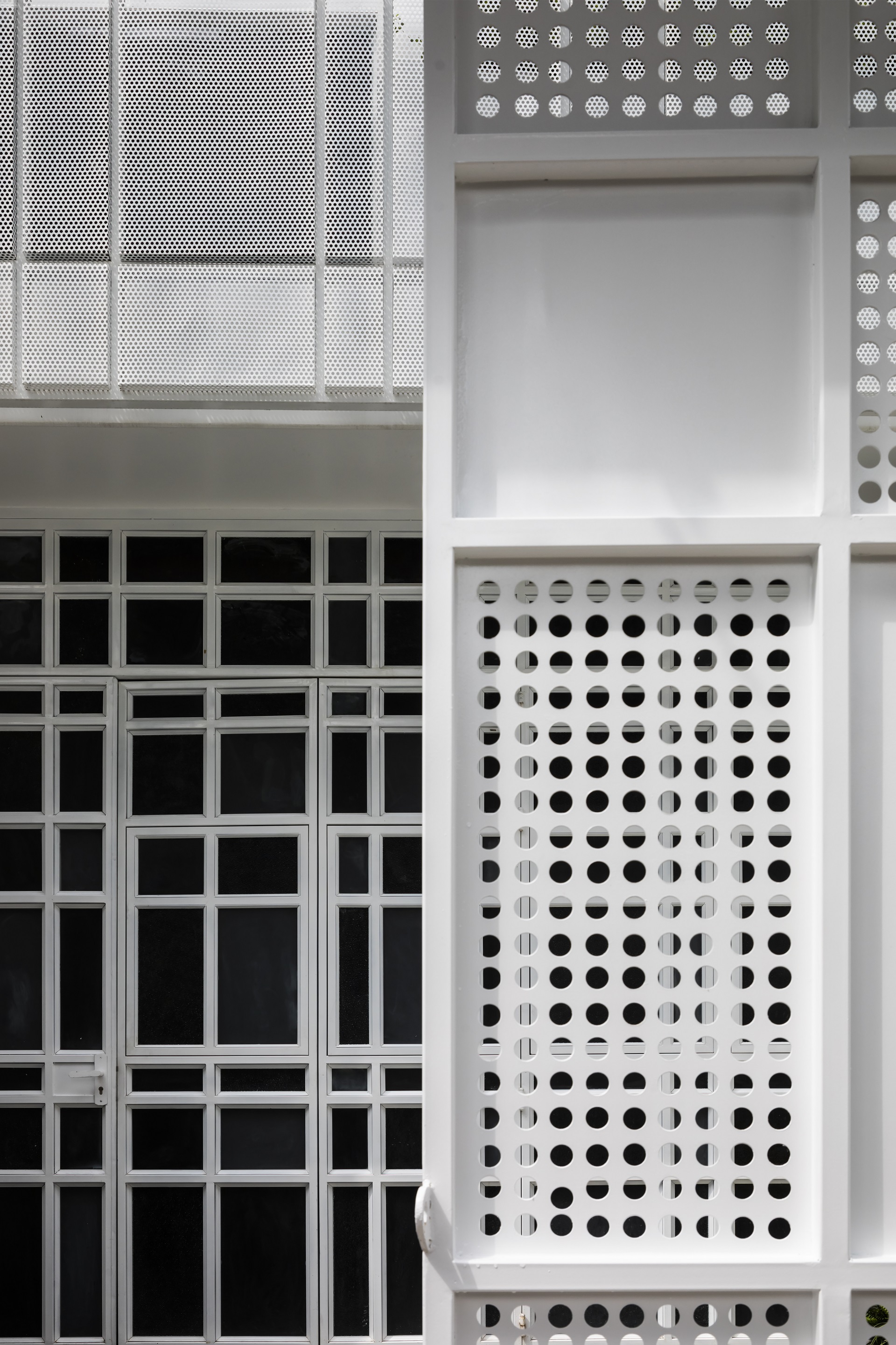 Close-up of white metal facade panels showing perforated and solid modules in a grid