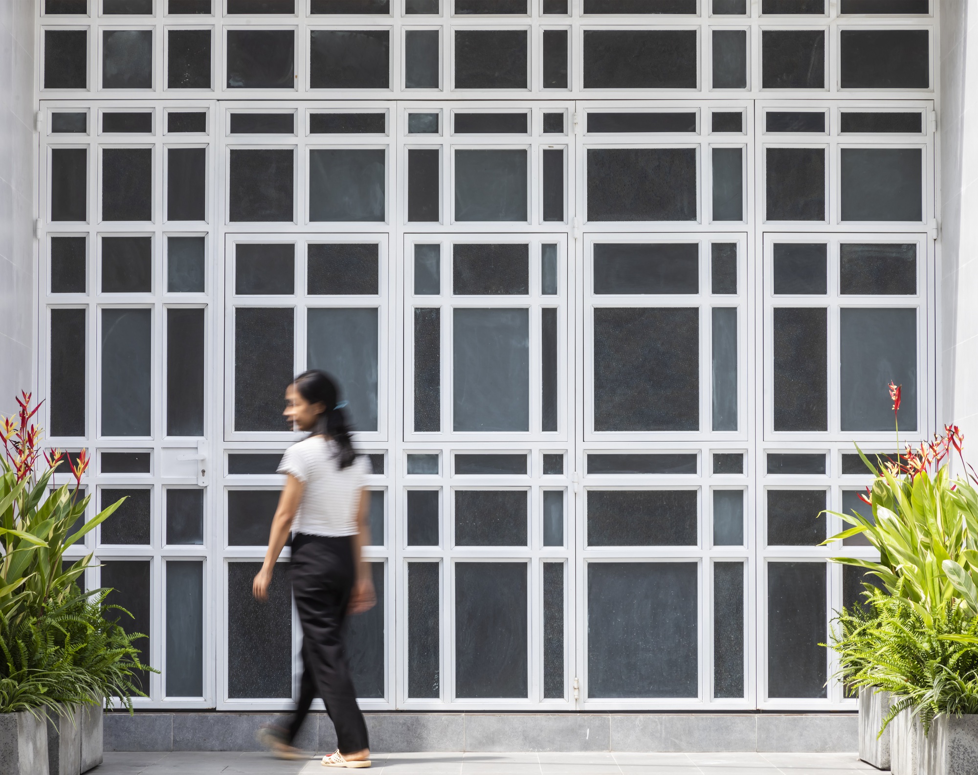 White gridded metal screen facade with a person walking past potted plants
