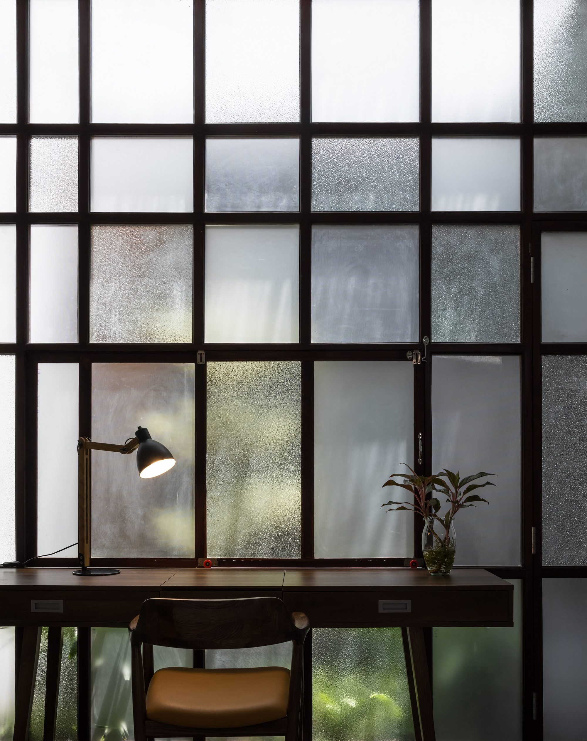 Desk with a lamp and plant against a translucent glass partition wall with dark frames